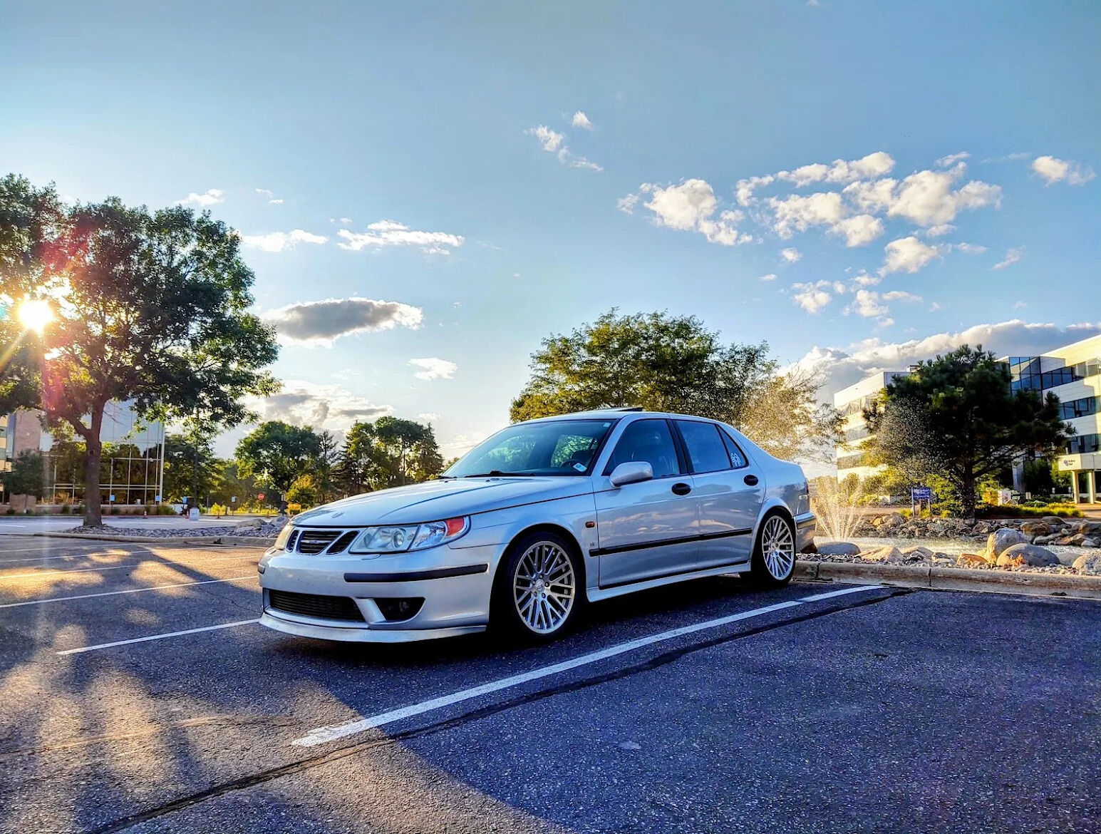 Silver Saab 9-3 sedan parked in a lot, with the sun shining in the background.