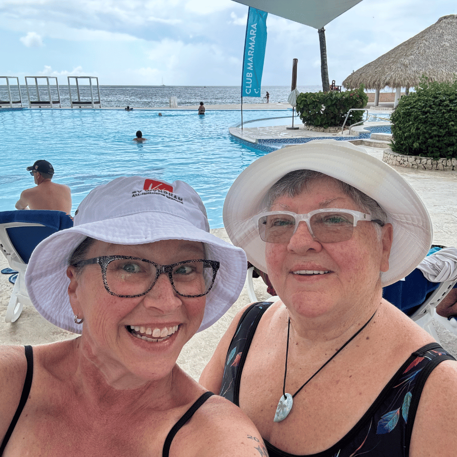 Two smiling people in sun hats at a resort pool with the ocean in the background.