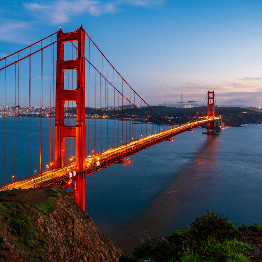 Person in orange blazer presents at a laptop-filled office meeting, with coworkers listening nearby.