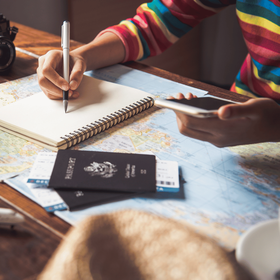 Traveler writing in a notebook beside a map and passports on a table
