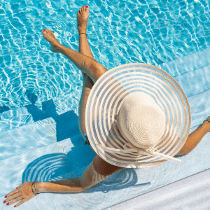 Woman relaxing on a pool float in bright blue water, wearing a wide-brimmed sunhat.