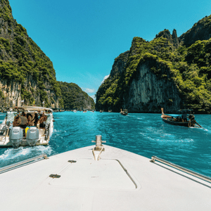 Speedboat view of turquoise water between steep green cliffs and boats in a tropical bay