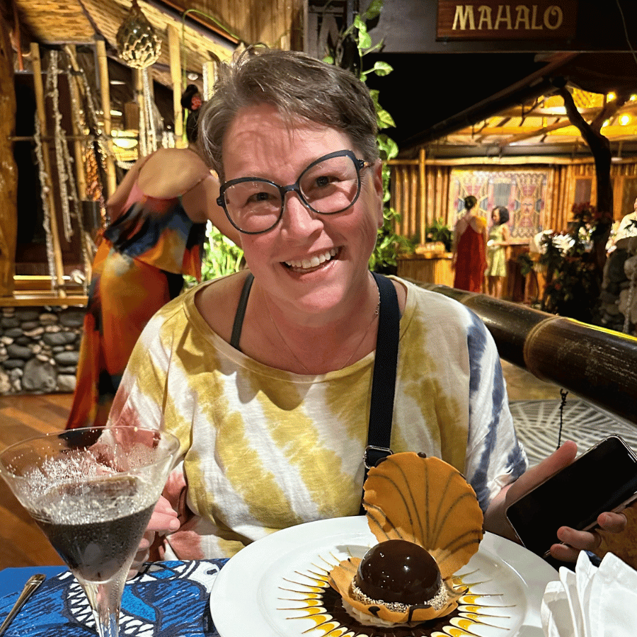 Smiling person at a tropical restaurant with a dessert and drink on the table
