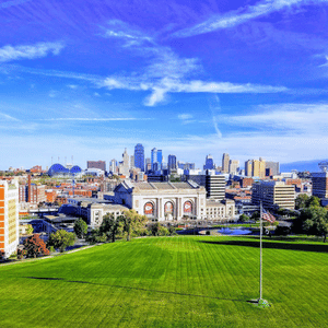 City skyline beyond a bright green park under a blue sky with wispy clouds