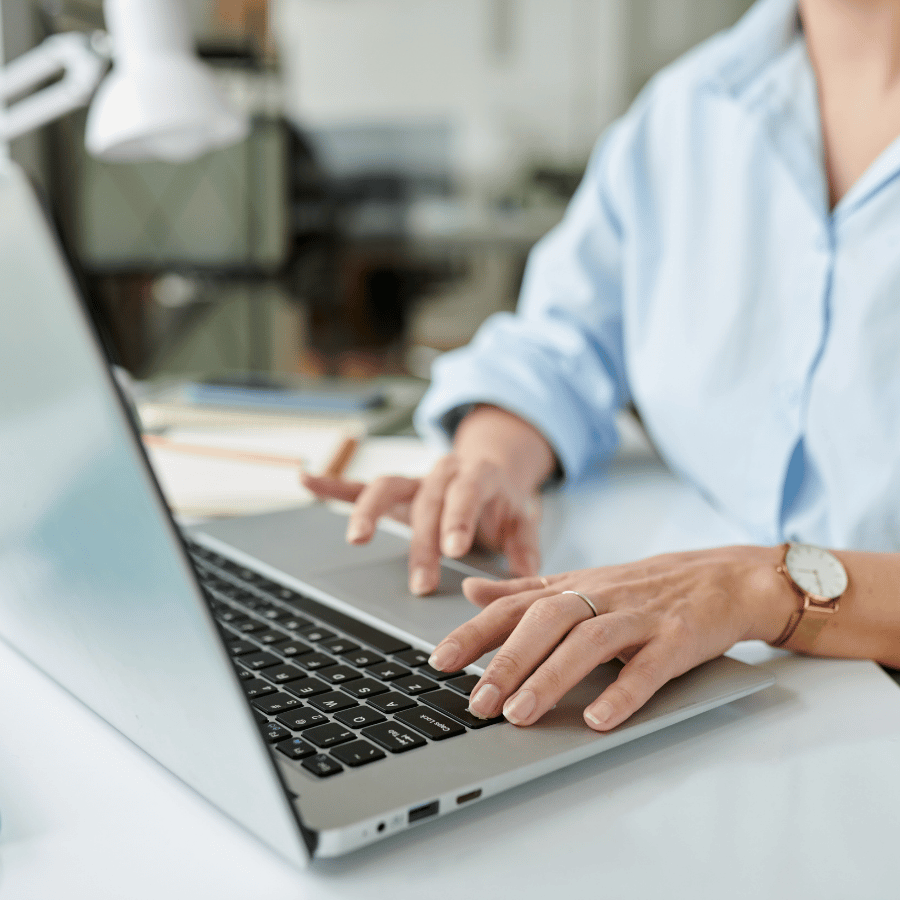 Person typing on a laptop at a desk, with a light blue shirt and wristwatch visible.