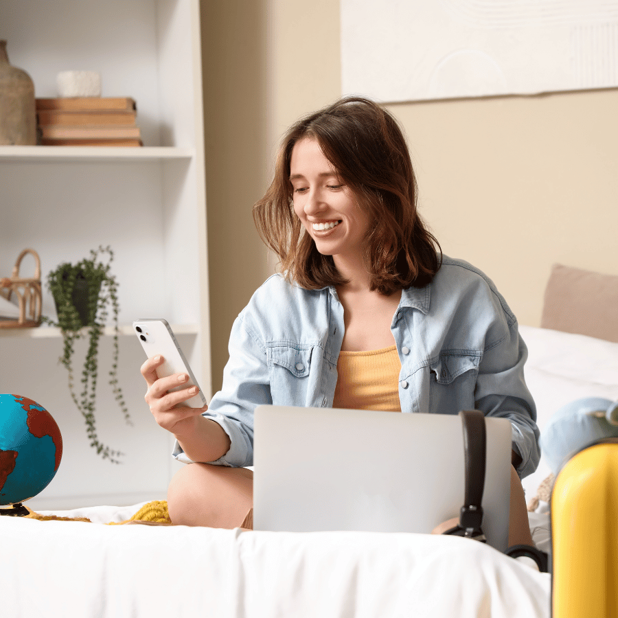 Woman smiling at a phone beside a laptop in a bright living room