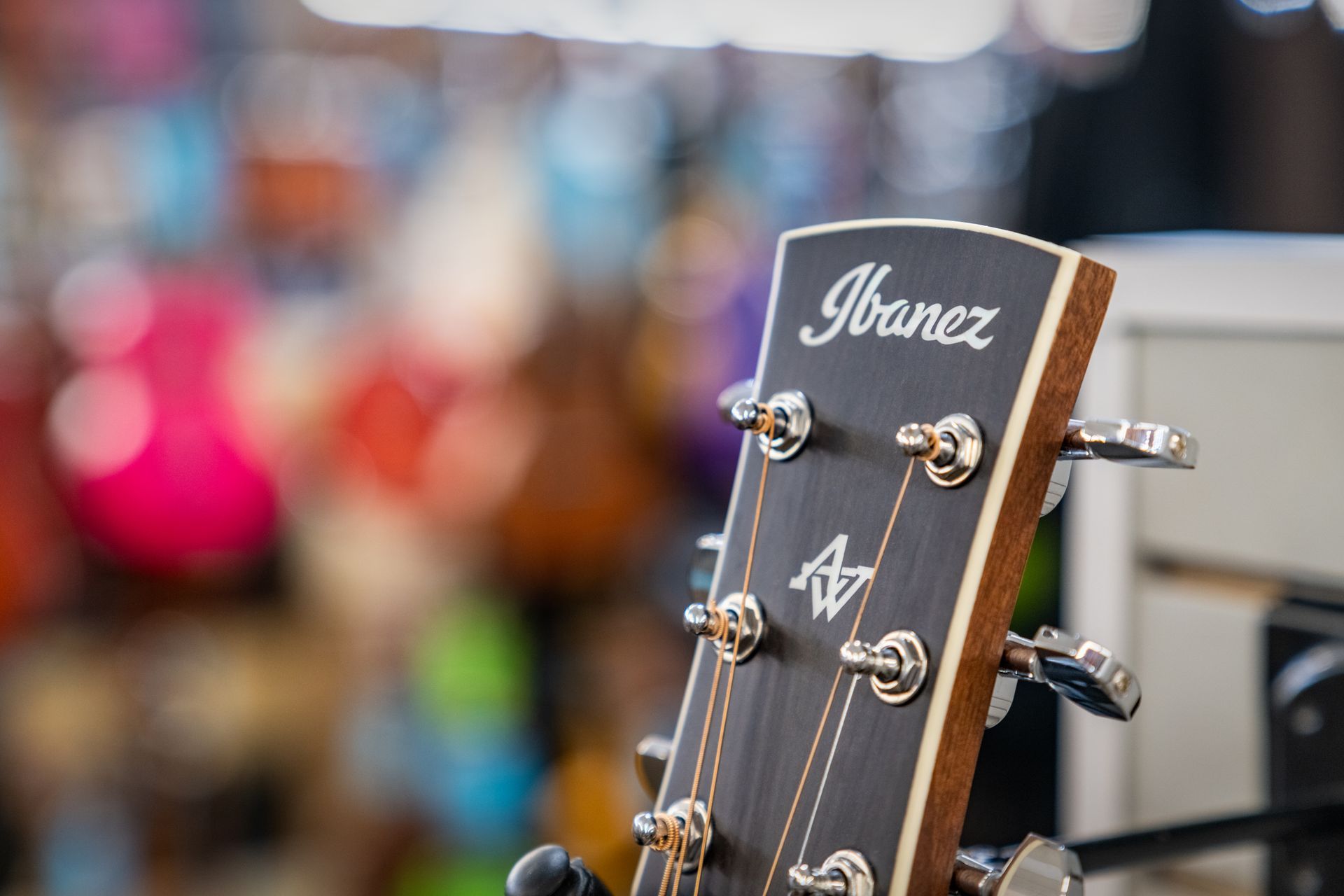 Ibanez acoustic guitar headstock with tuning pegs, logo. In a music store with blurred guitar background.