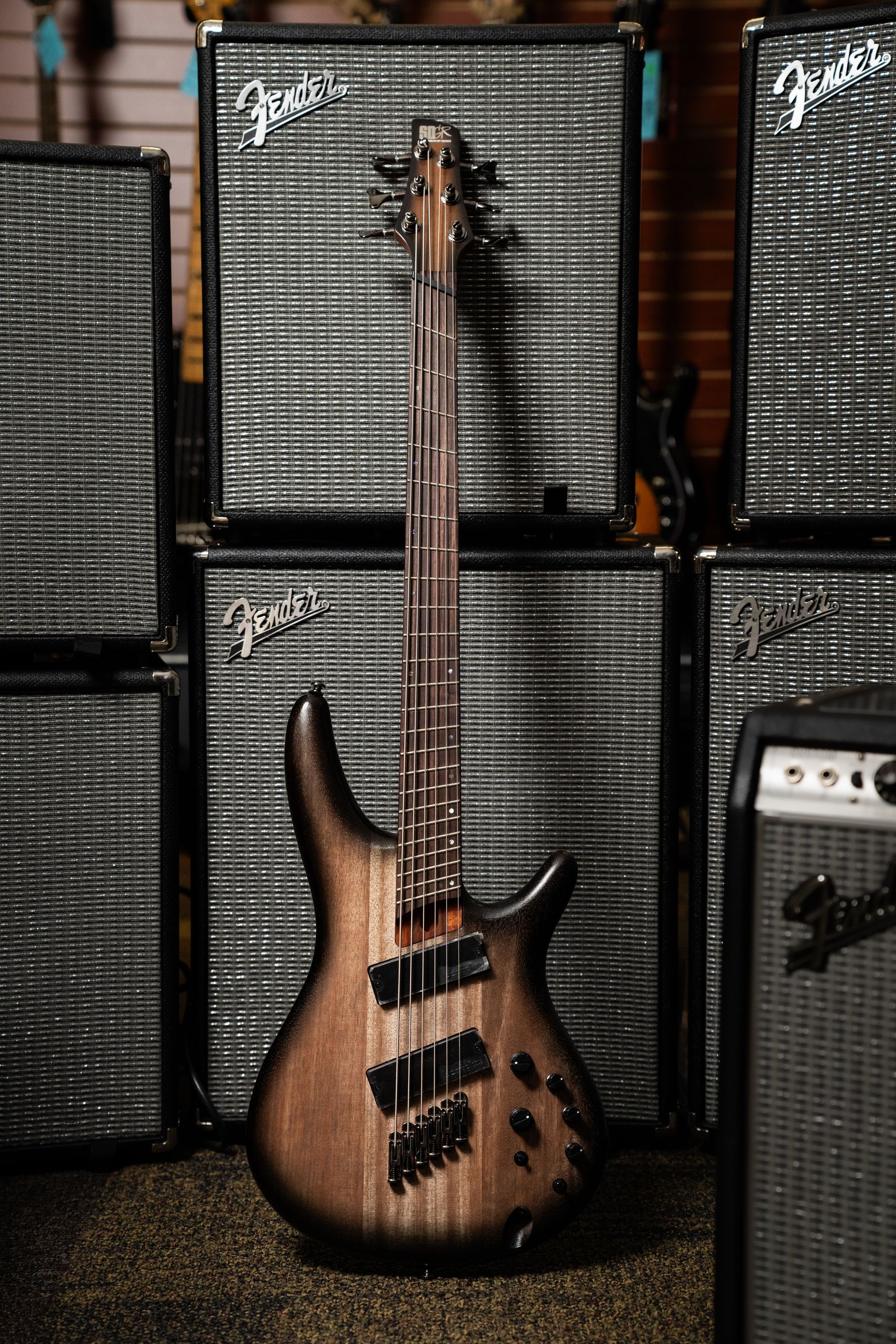 Brown bass guitar in front of a wall of amplifiers.