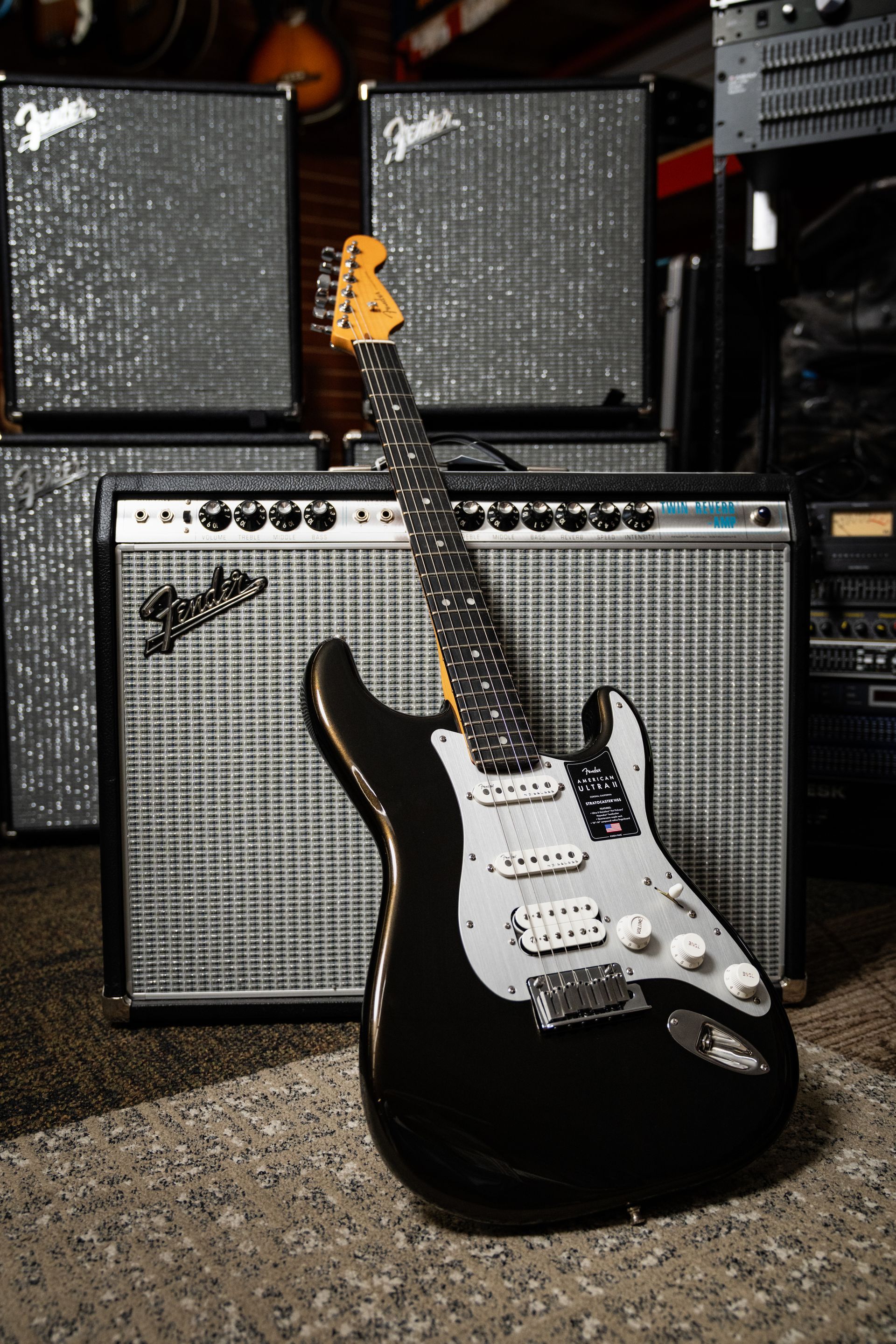 Black electric guitar leaning against a silver Fender amplifier stack.