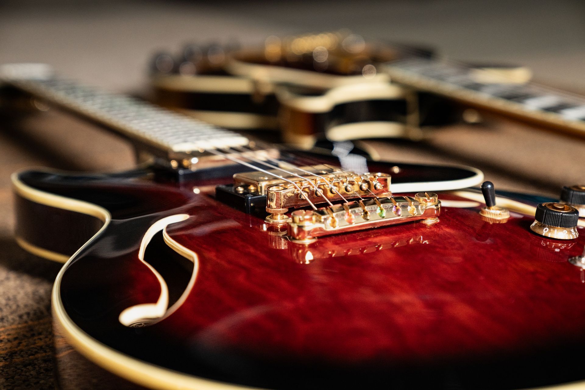 Three dark red electric guitars, one in focus with gold hardware, on a wooden surface.