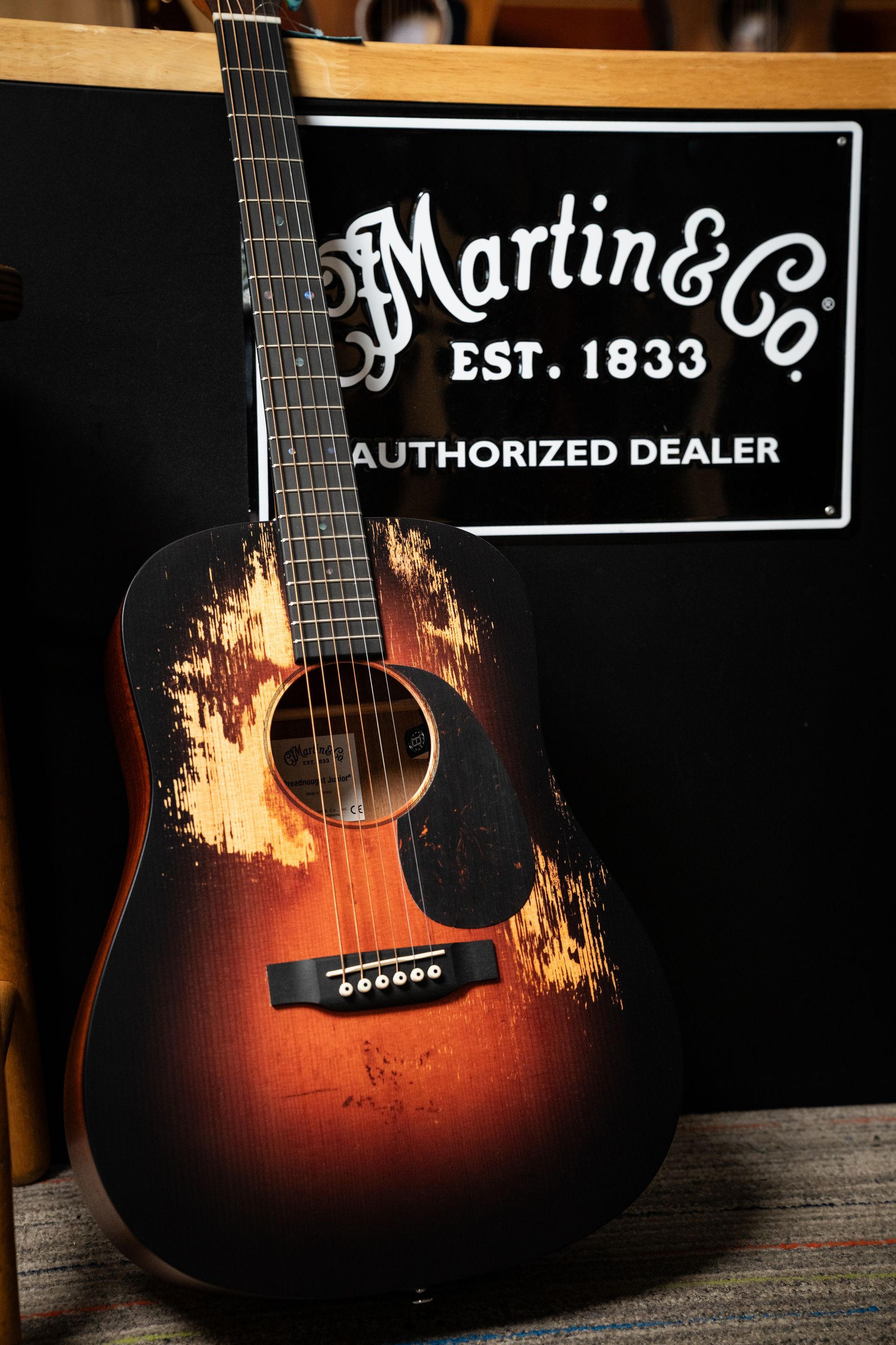 Acoustic Martin & Co. guitar with distressed finish, leaning against a sign.