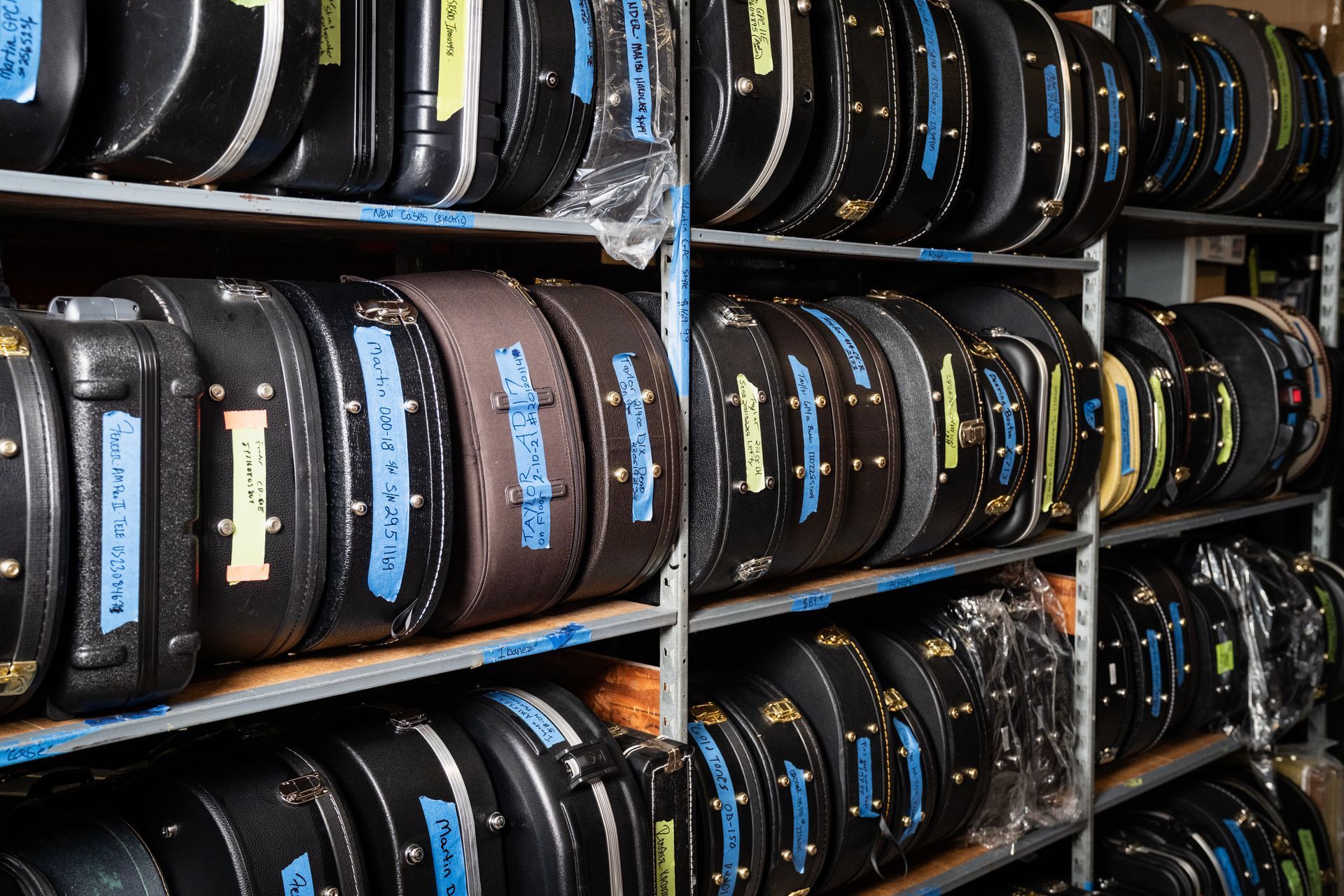 Shelves filled with black guitar cases, many labeled with blue and yellow tape.