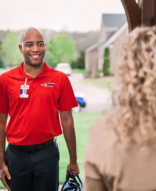 Man in red shirt smiling, holding bag, facing person at doorway.