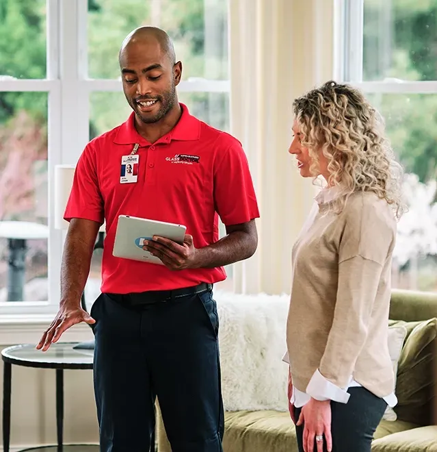 A man in a red polo shirt explains something on a tablet to a woman in a living room.