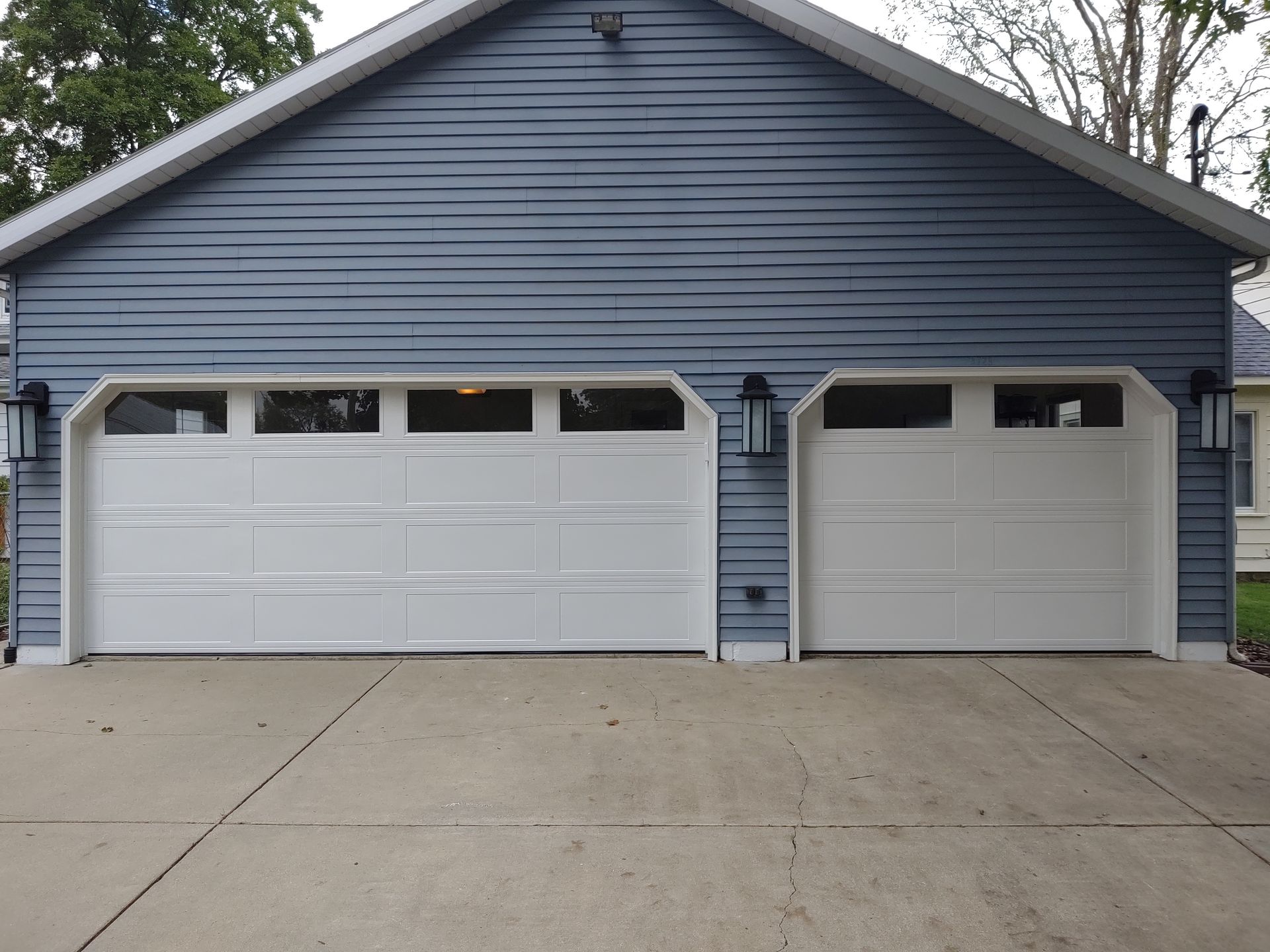 Blue house with two white garage doors and a wide concrete driveway