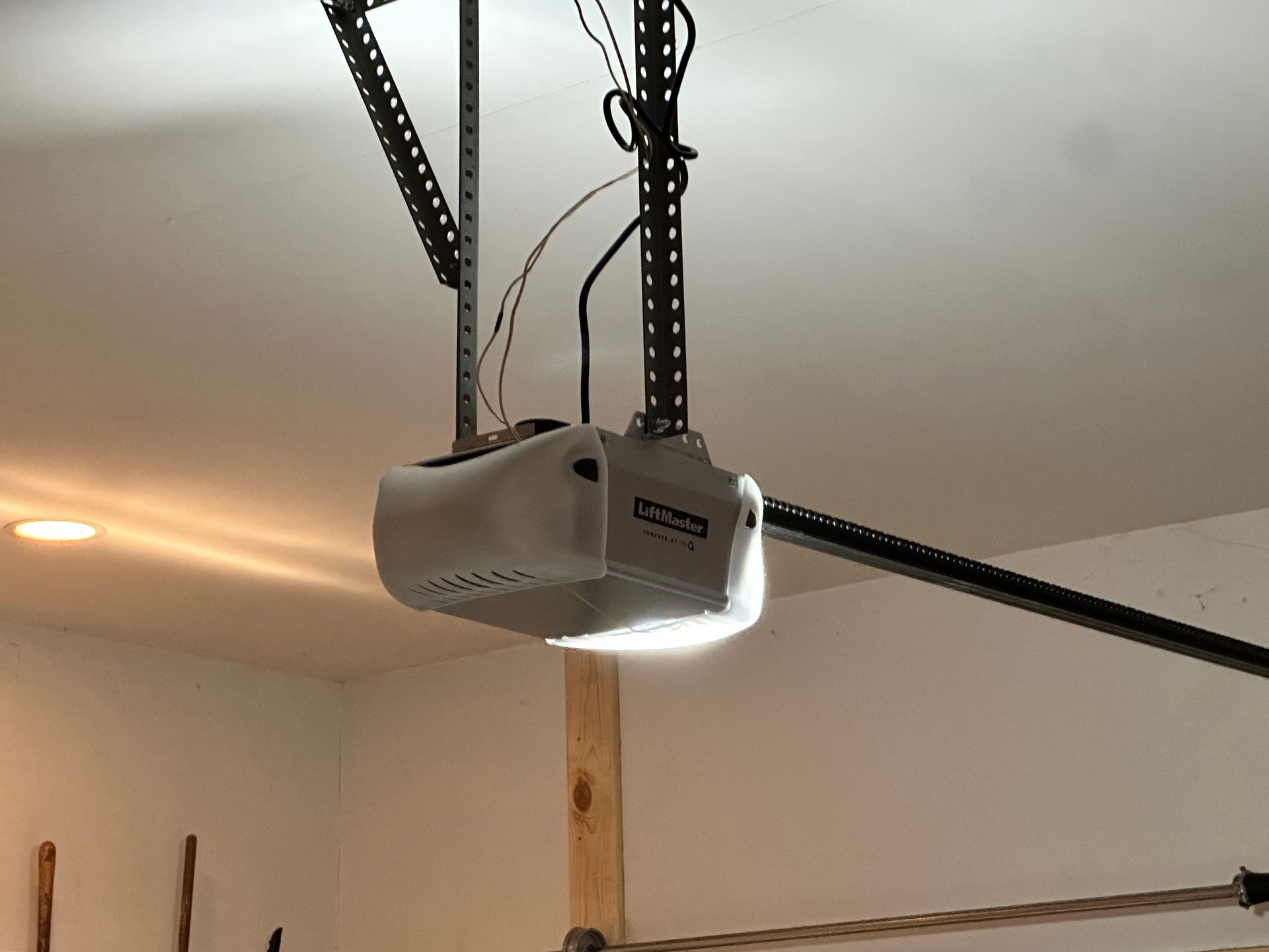 White ceiling-mounted garage door opener with black track rails and a lit garage ceiling.