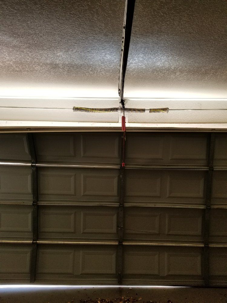 Closed garage door with a long crack across the upper panel and a red center support strap