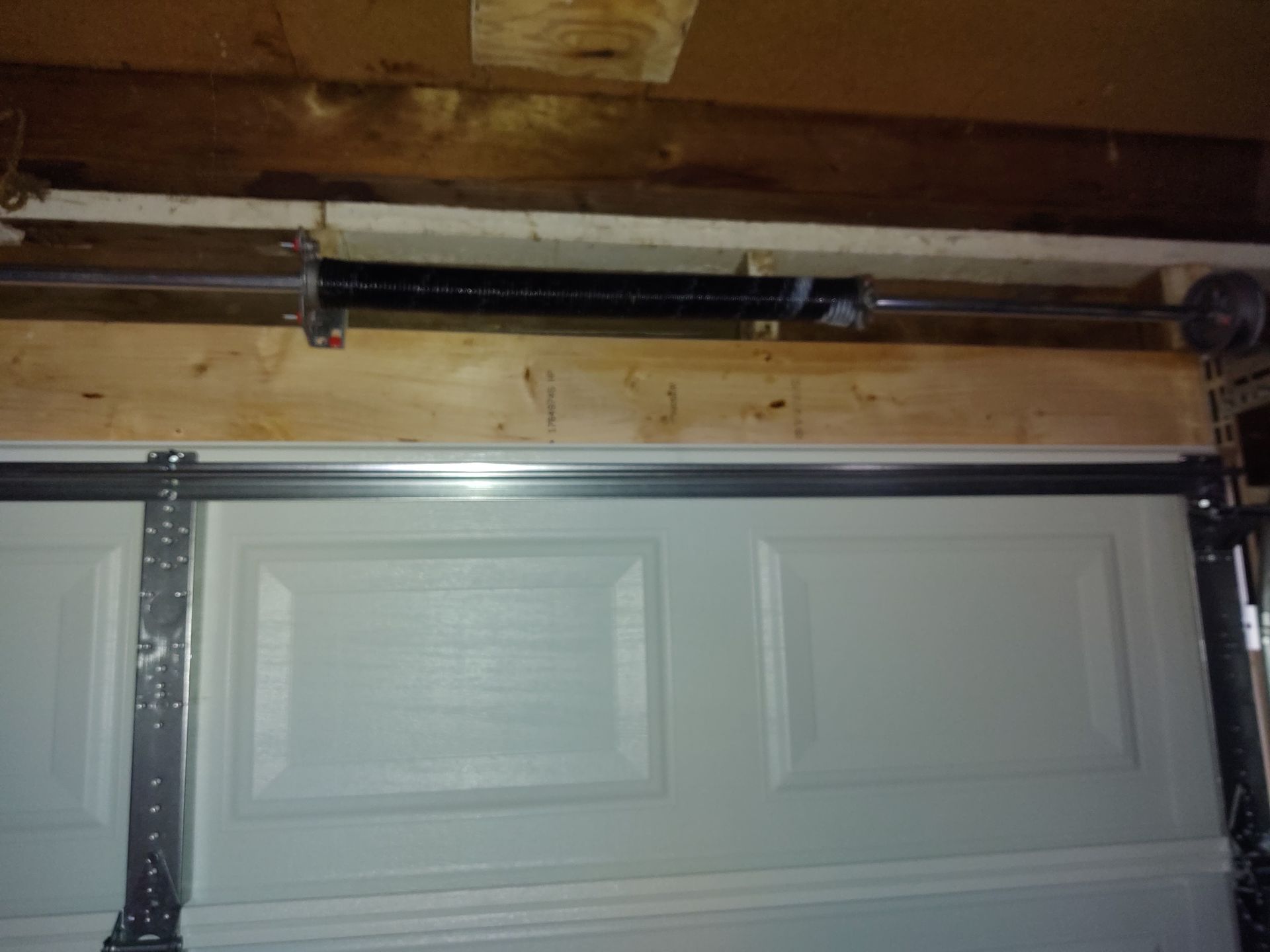 Garage door with visible overhead track, opener rail, and wooden ceiling framing above.