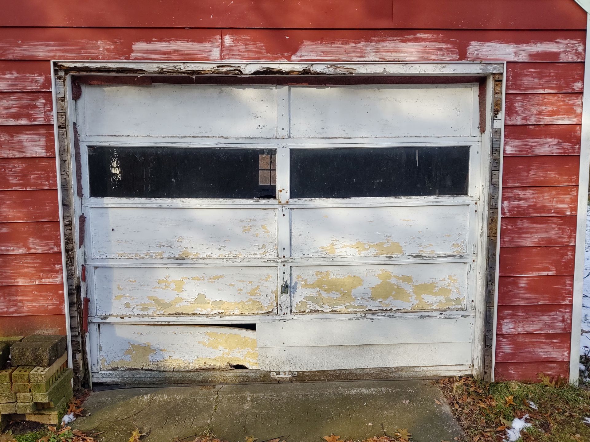 Weathered white garage door on a red wooden building, with peeling paint and dark windows.