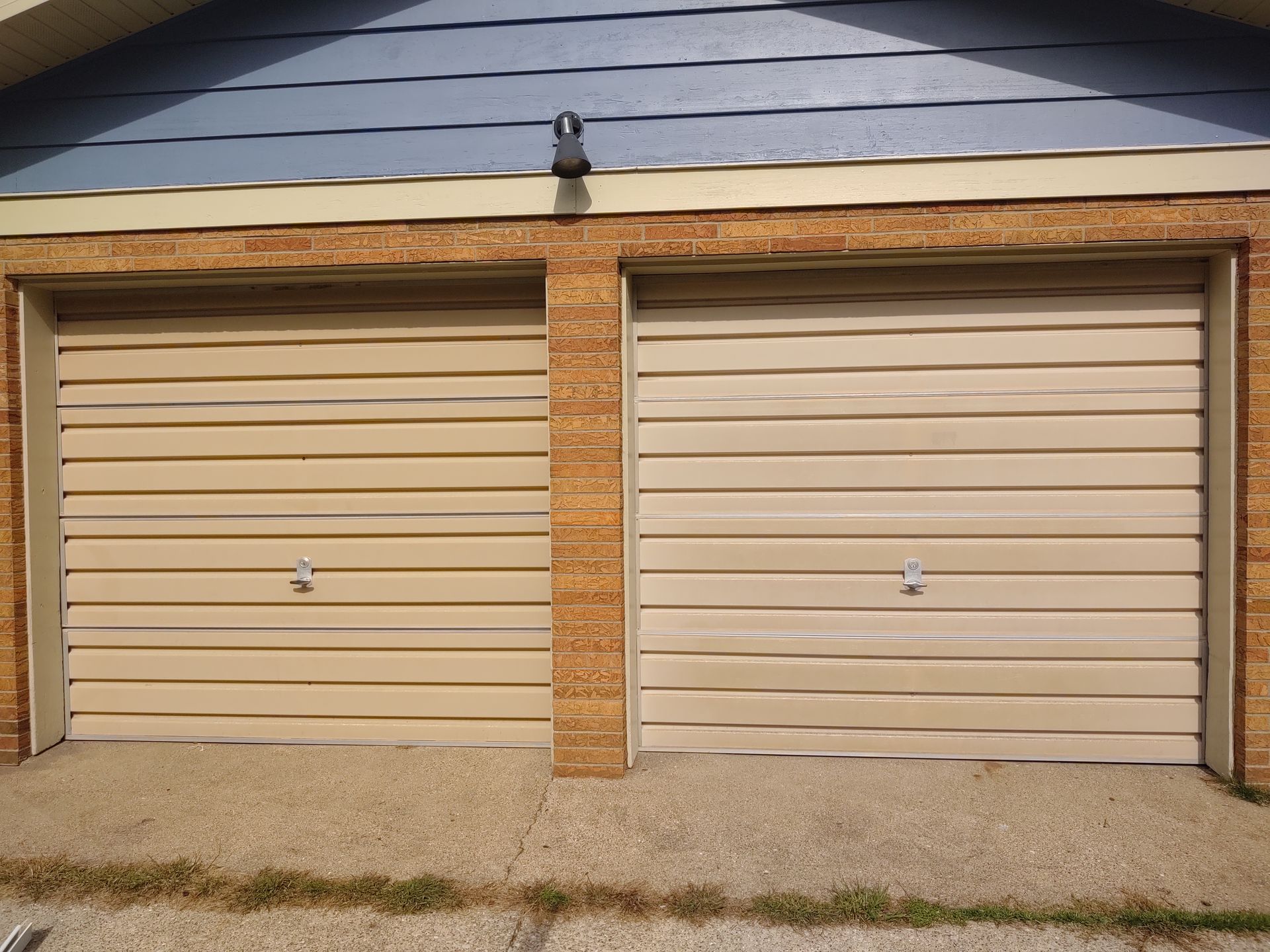Two beige garage doors with horizontal siding under a gray shingled roof