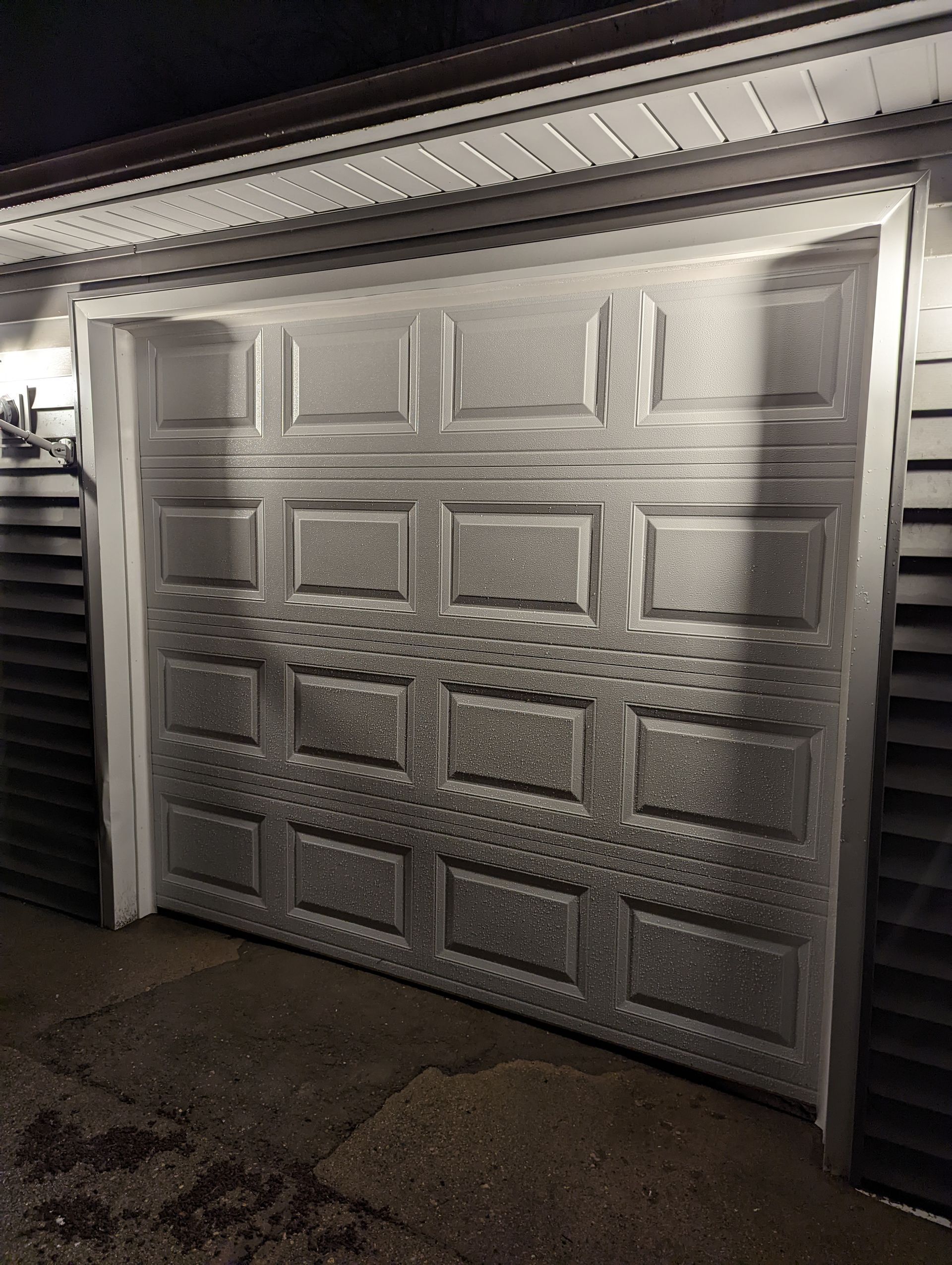 Closed white garage door with frosted lower panels at night, wet driveway in front