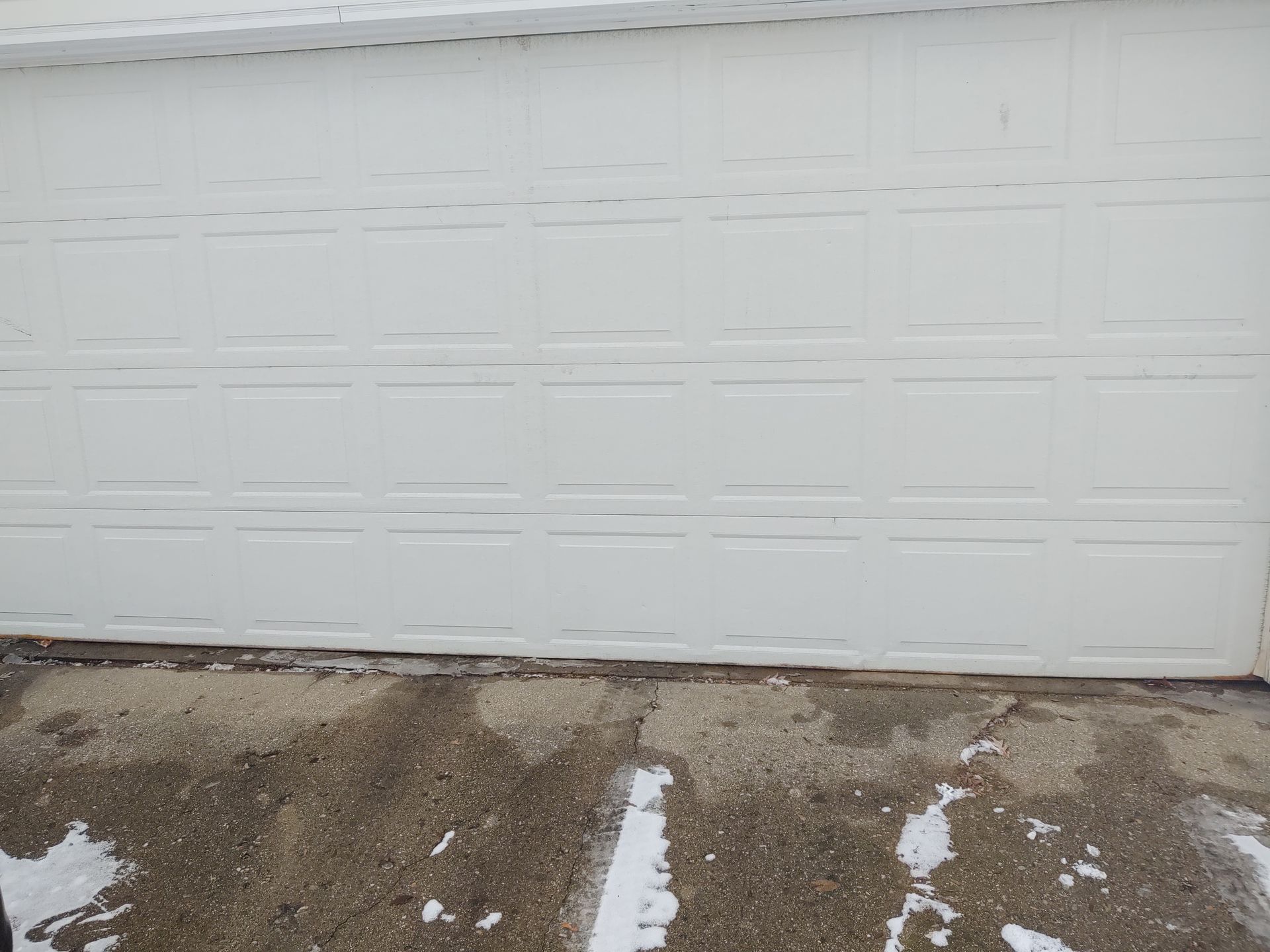 White garage door with horizontal panels above a muddy driveway with small patches of snow.