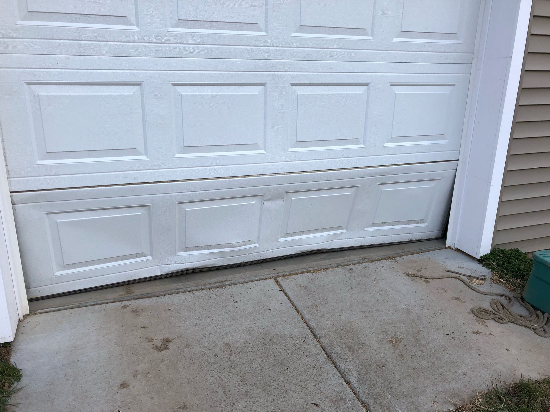 White garage door with a damaged bottom panel above a concrete driveway
