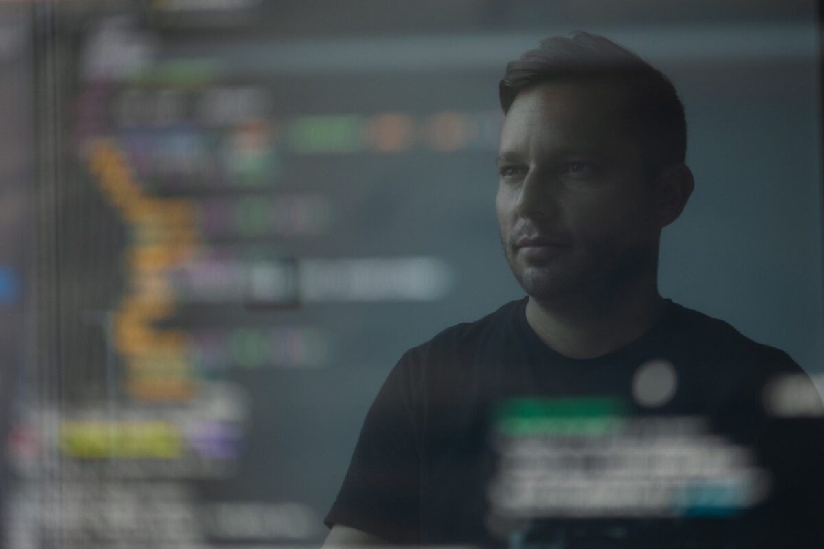 Man looking at a computer screen displaying code. Dark room. Focus on the man.