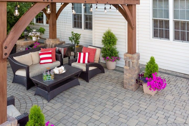 A patio with dark wicker outdoor furniture, red-and-white striped pillows, a coffee table, and potted plants under a pergola.