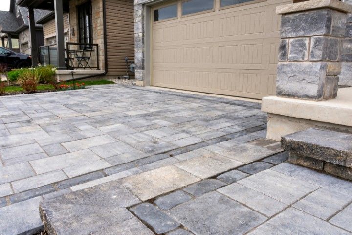 A paved residential driveway and walkway made of grey rectangular stone pavers leading to a beige garage door.