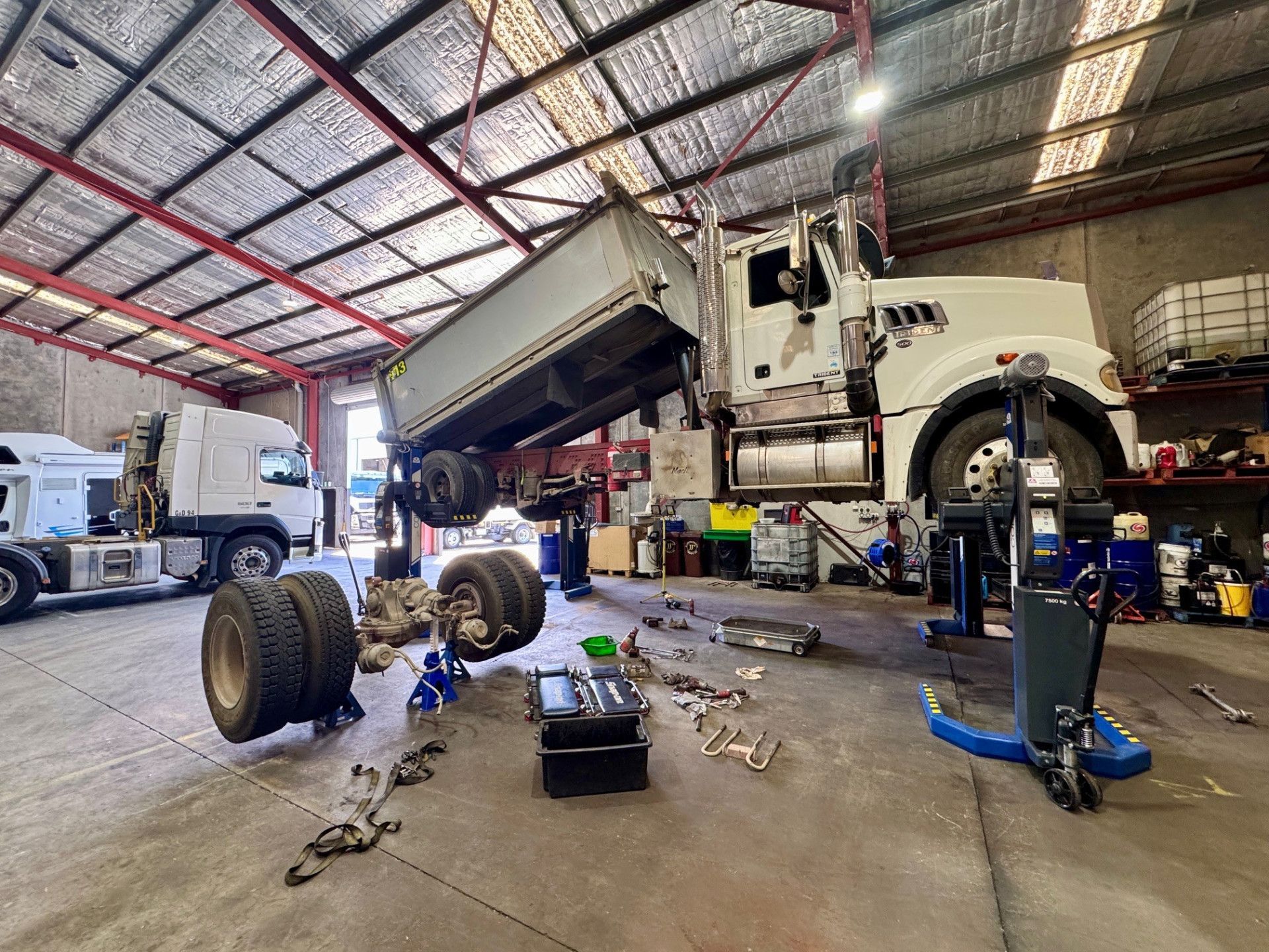 An Orange Dump Truck is on a Lift in a Garage — Inline Truck and Plant in Tuggerah, NSW