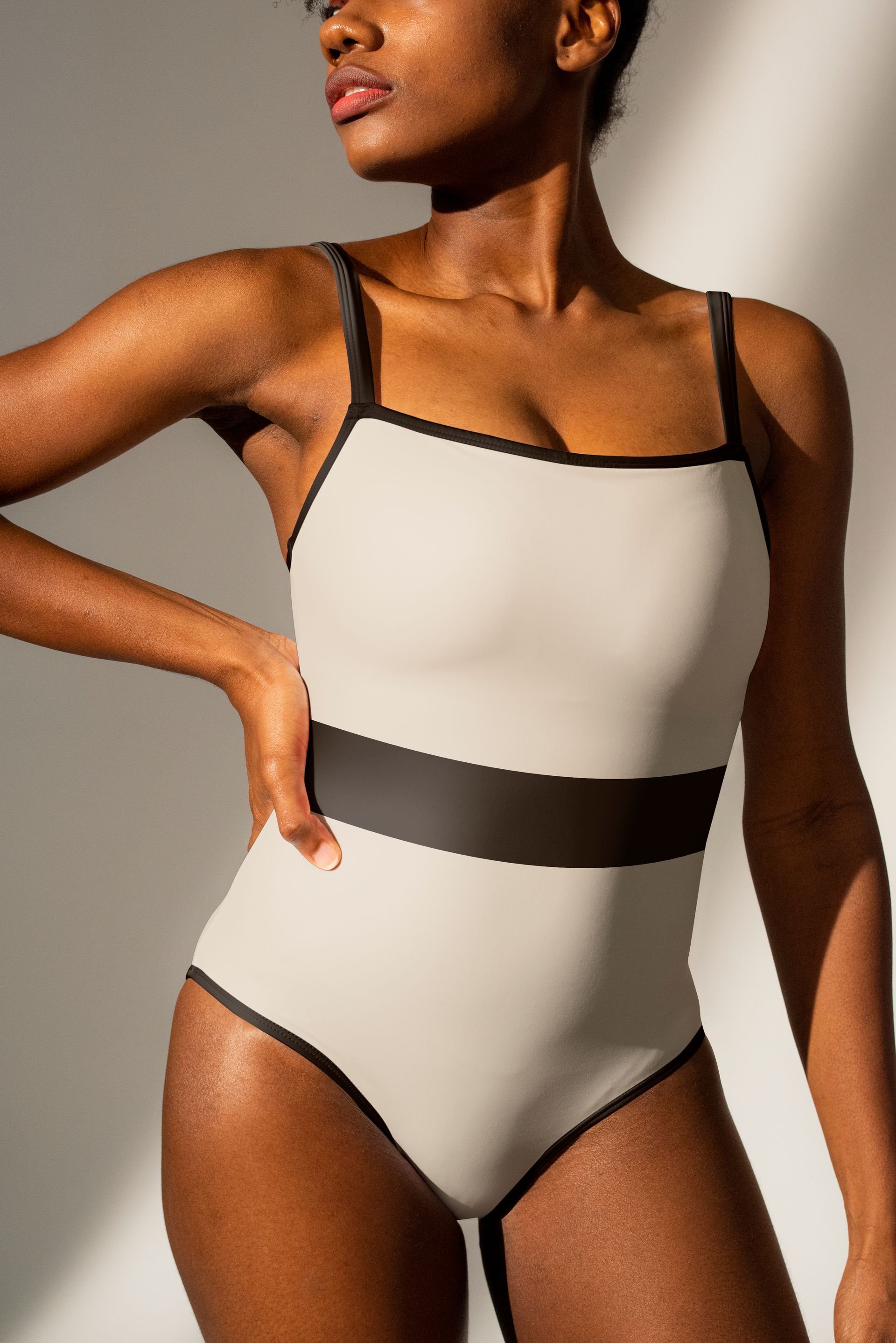 A woman in a white and black swimsuit is standing in front of a white wall.