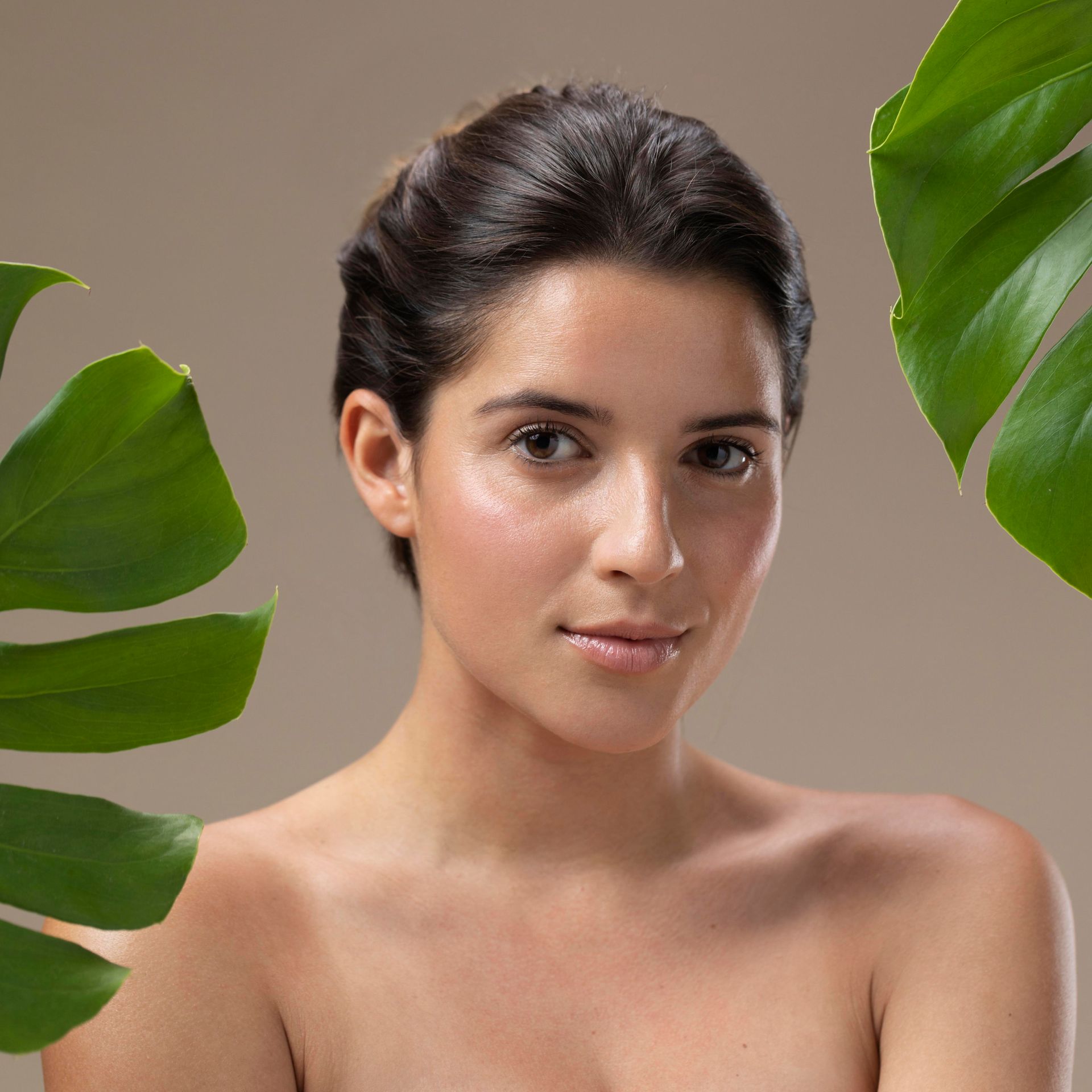 A woman without a shirt is surrounded by green leaves.