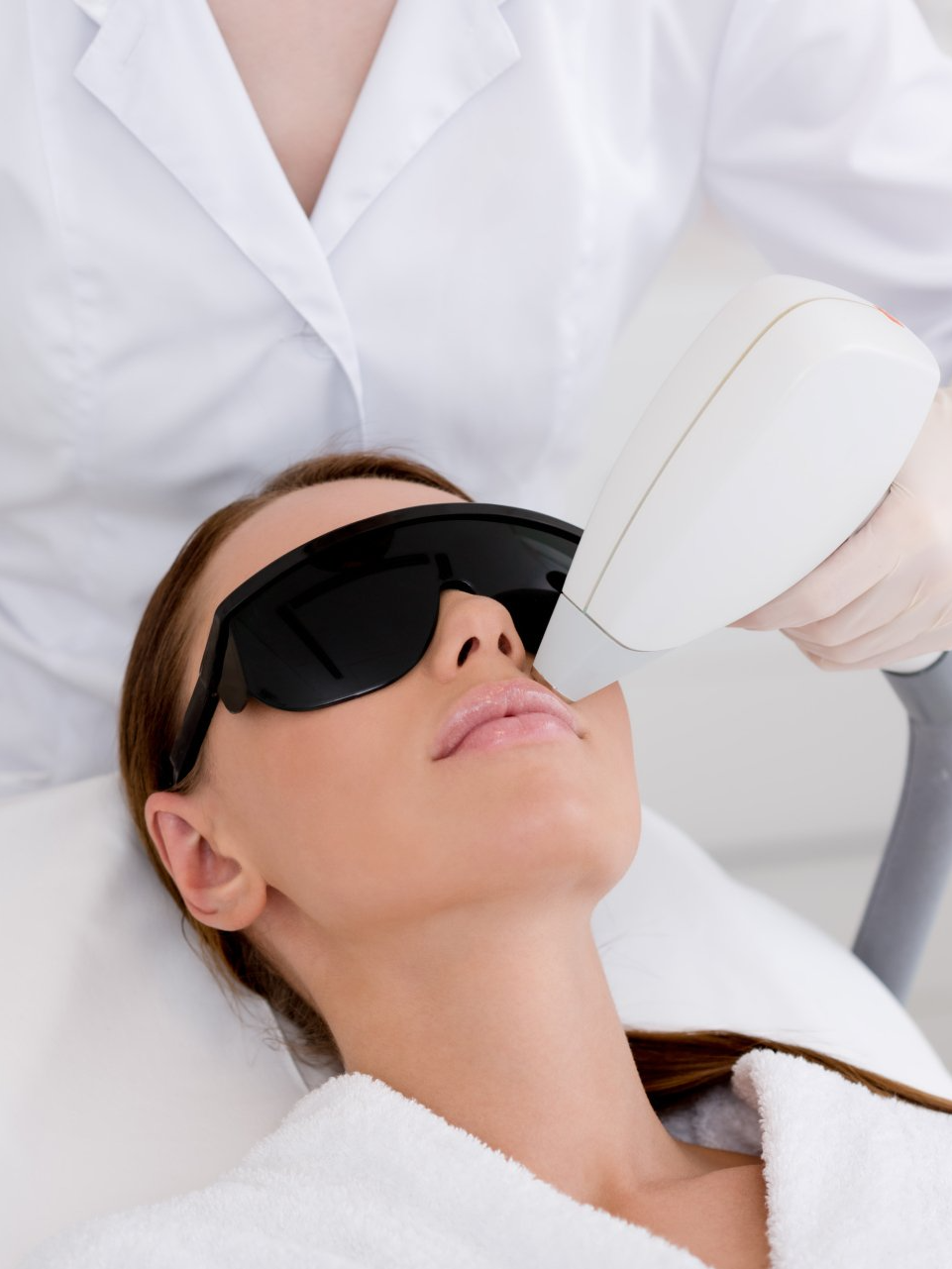 A woman wearing sunglasses is getting a laser treatment on her face.