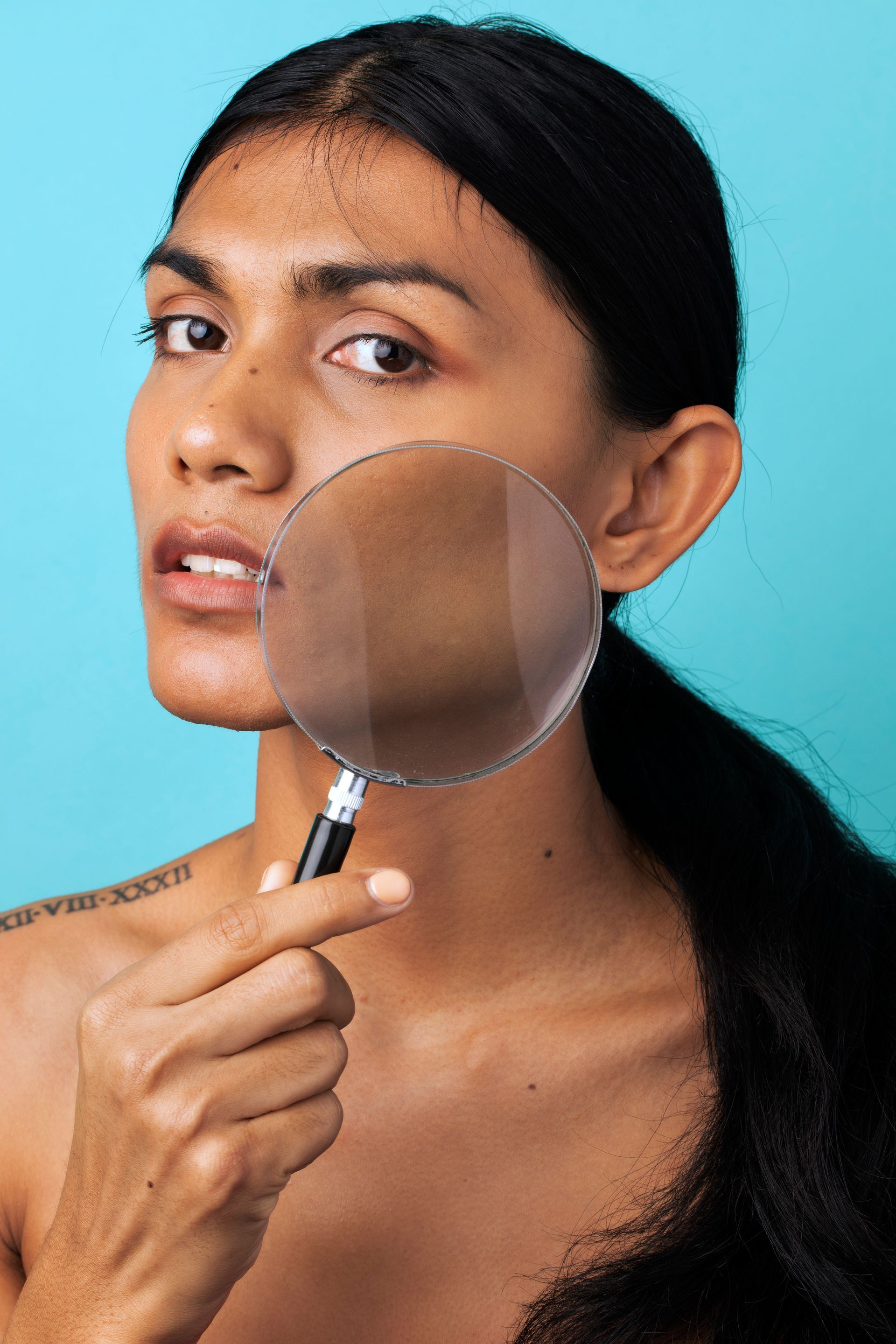 A woman is looking at her face through a magnifying glass.