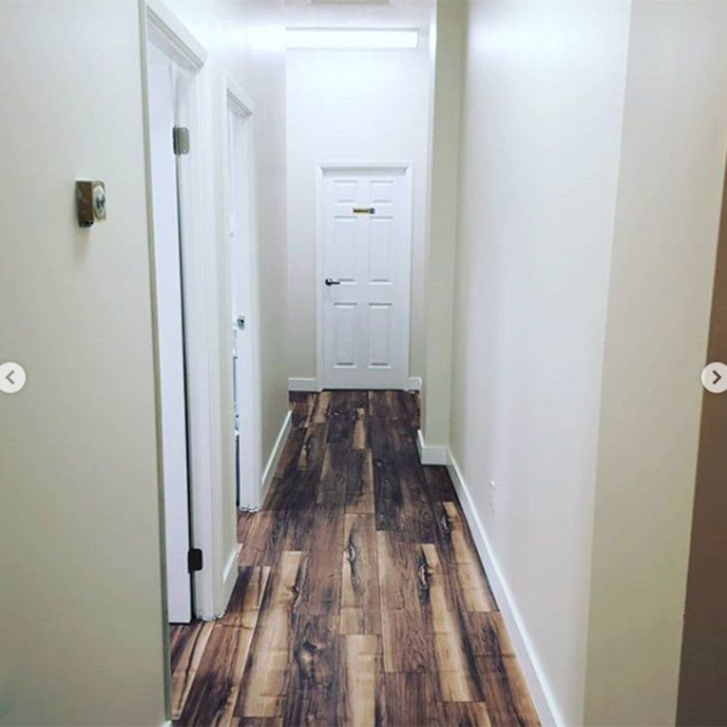 A long hallway with wooden floors and white walls leading to a door.