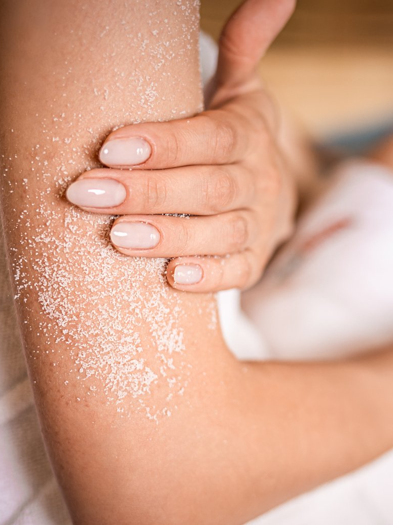 A woman is applying a body scrub to her elbow.