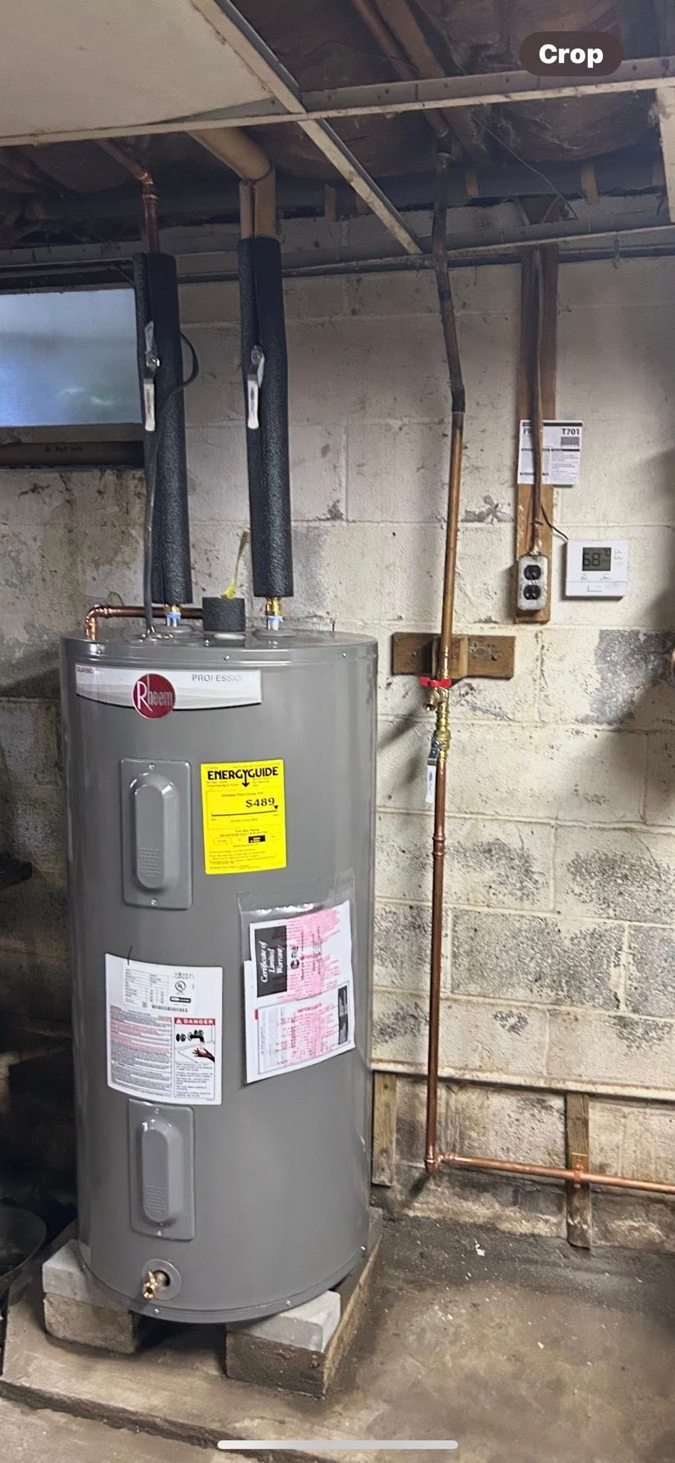 A gray electric water heater installed in a basement, standing on concrete blocks with exposed copper plumbing above.