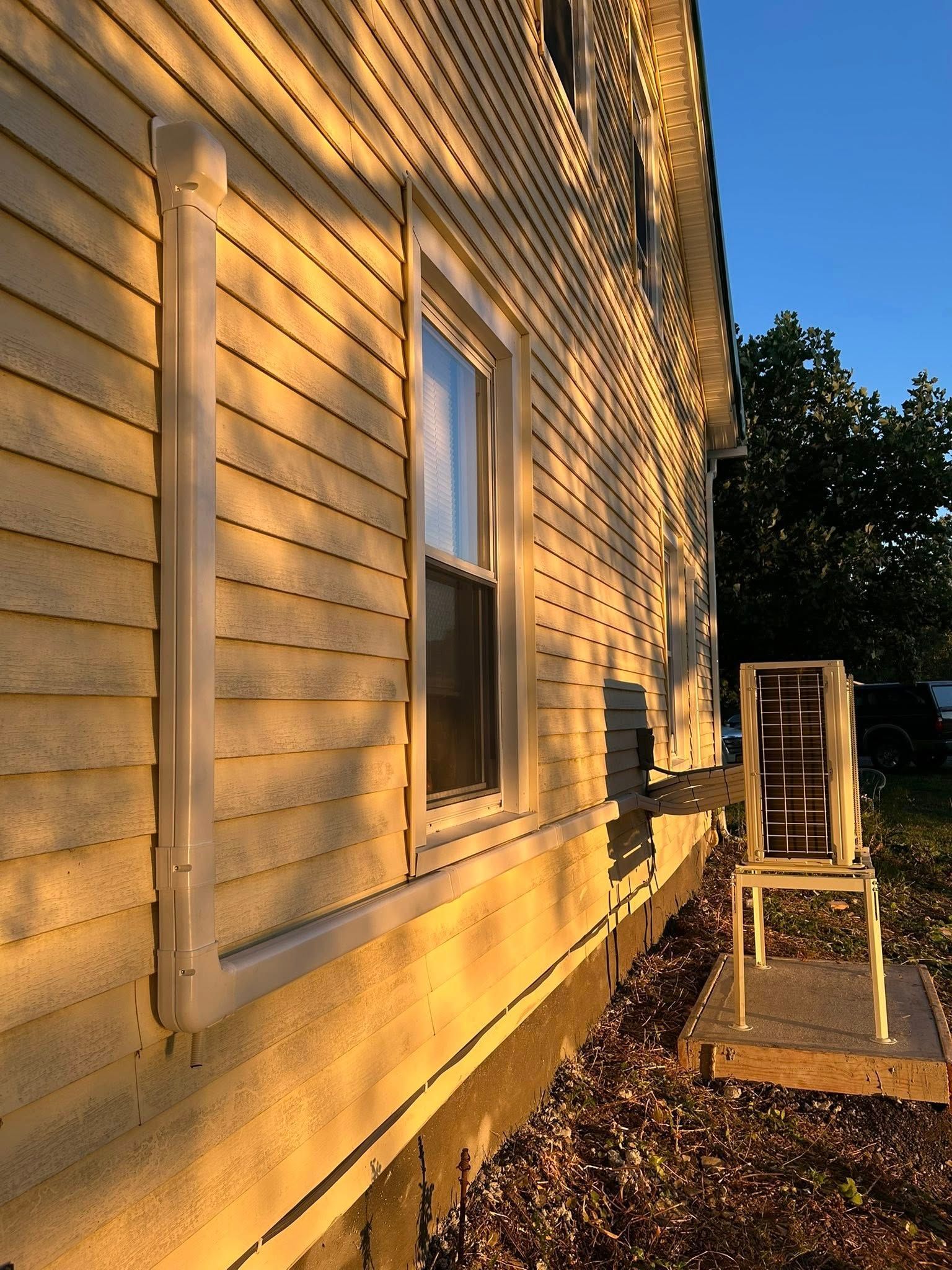 A yellow house exterior with a white conduit line along the siding, leading to an HVAC unit on a stand in the yard.
