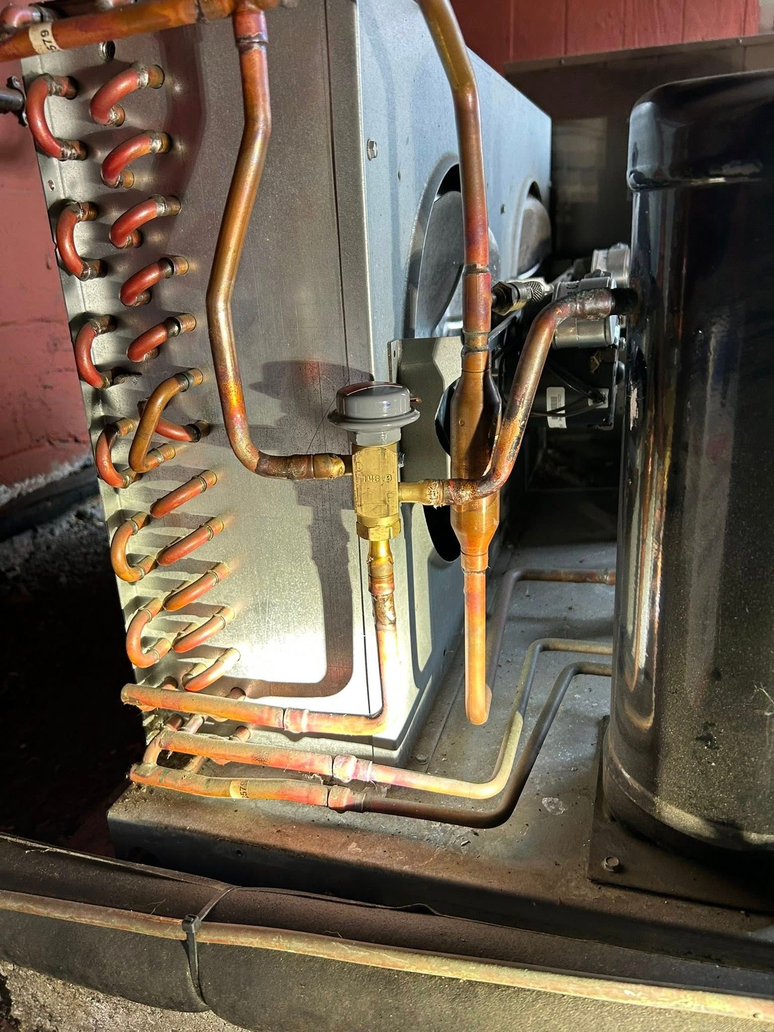 Close-up of refrigeration unit piping, copper tubing, and a brass expansion valve mounted on a metal condenser coil.