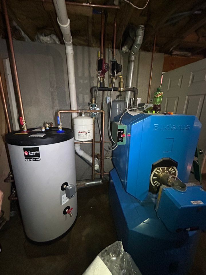 A residential mechanical room featuring a light gray indirect water heater beside a large blue oil-fired boiler.