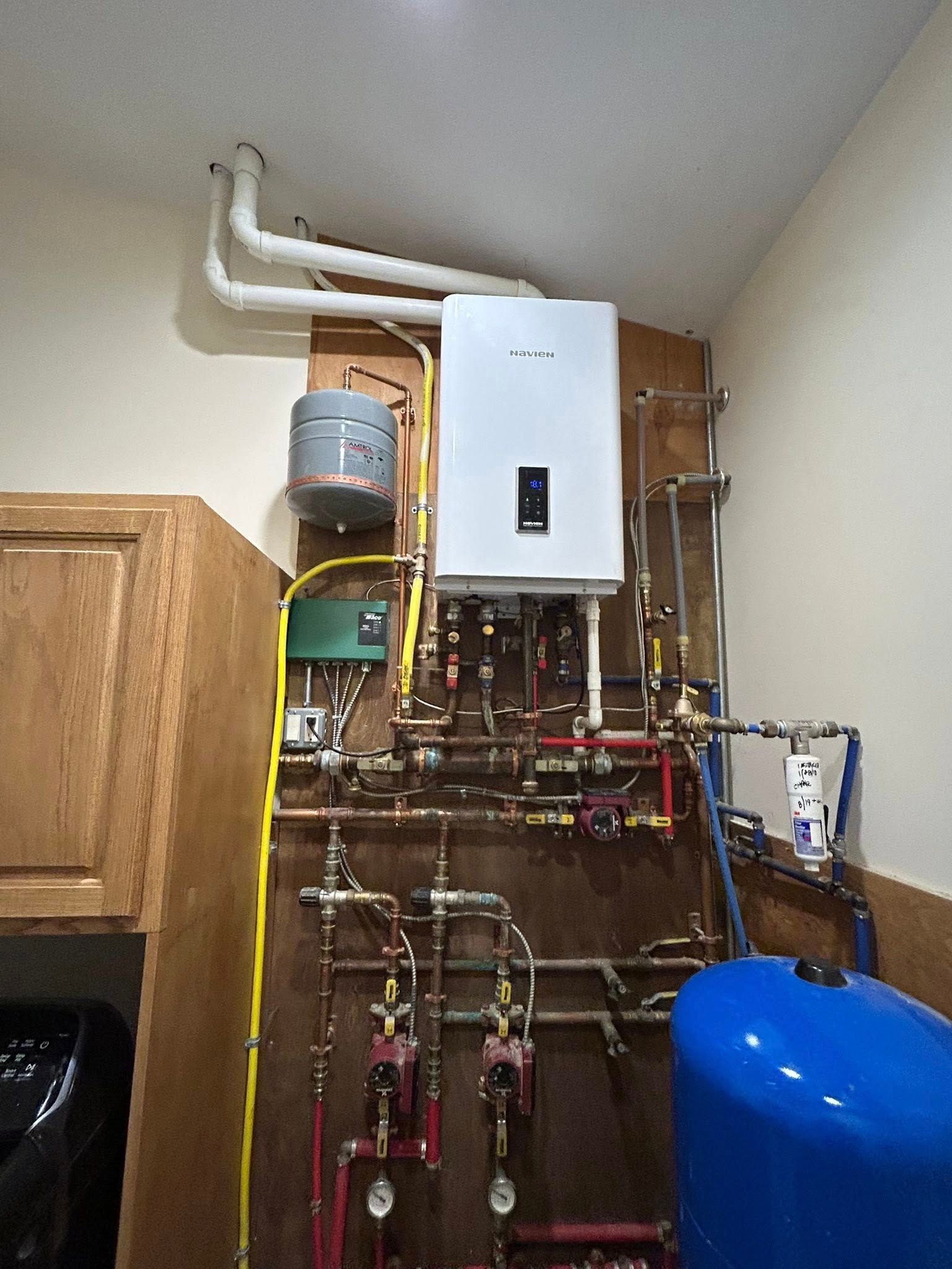 Wall-mounted gas boiler, piping, and blue pressure tank installed in a utility space.