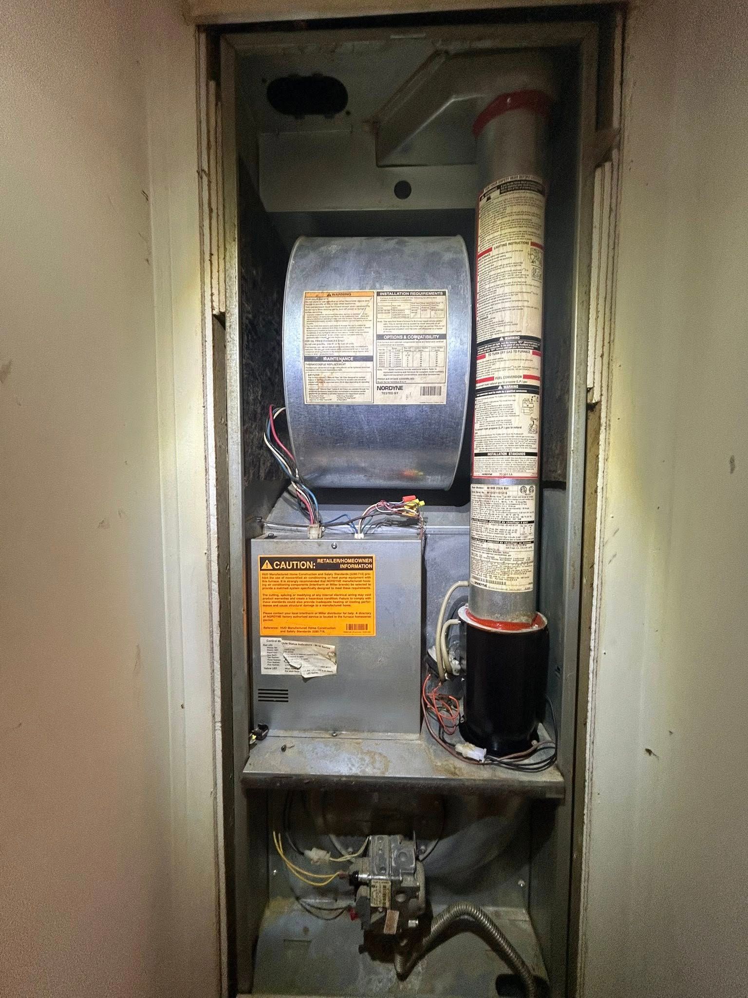 A residential heating and cooling unit housed in a vertical utility closet, showing internal components and metal ducting.