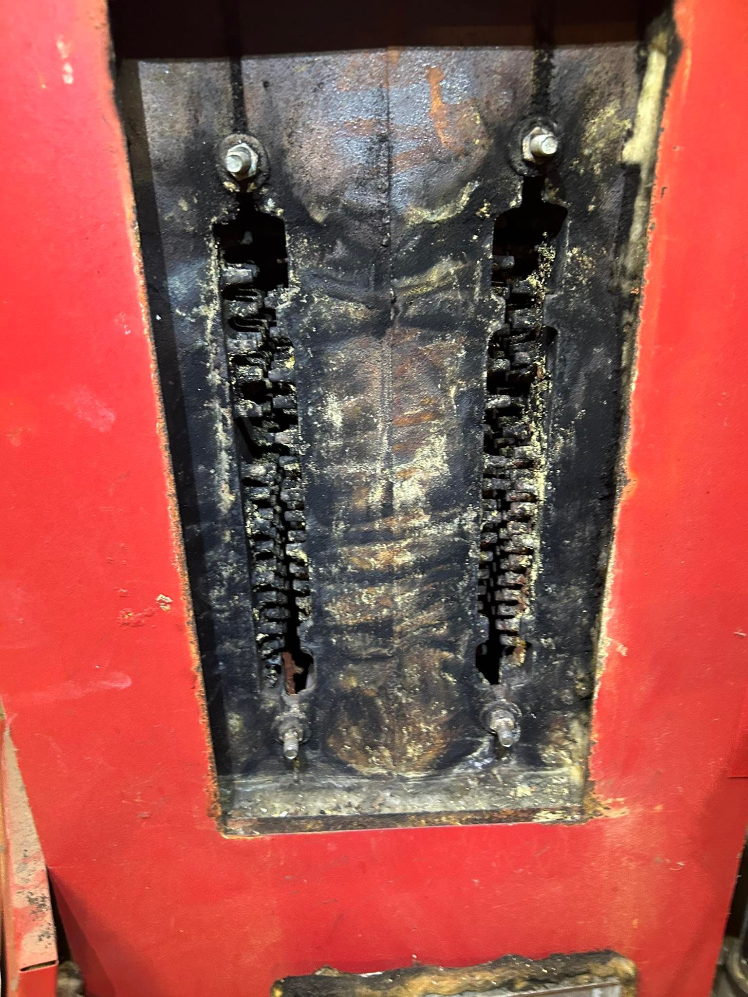 A close-up of a rustic, red wood-burning stove with two vertical rows of decorative metal grillwork covered in soot.