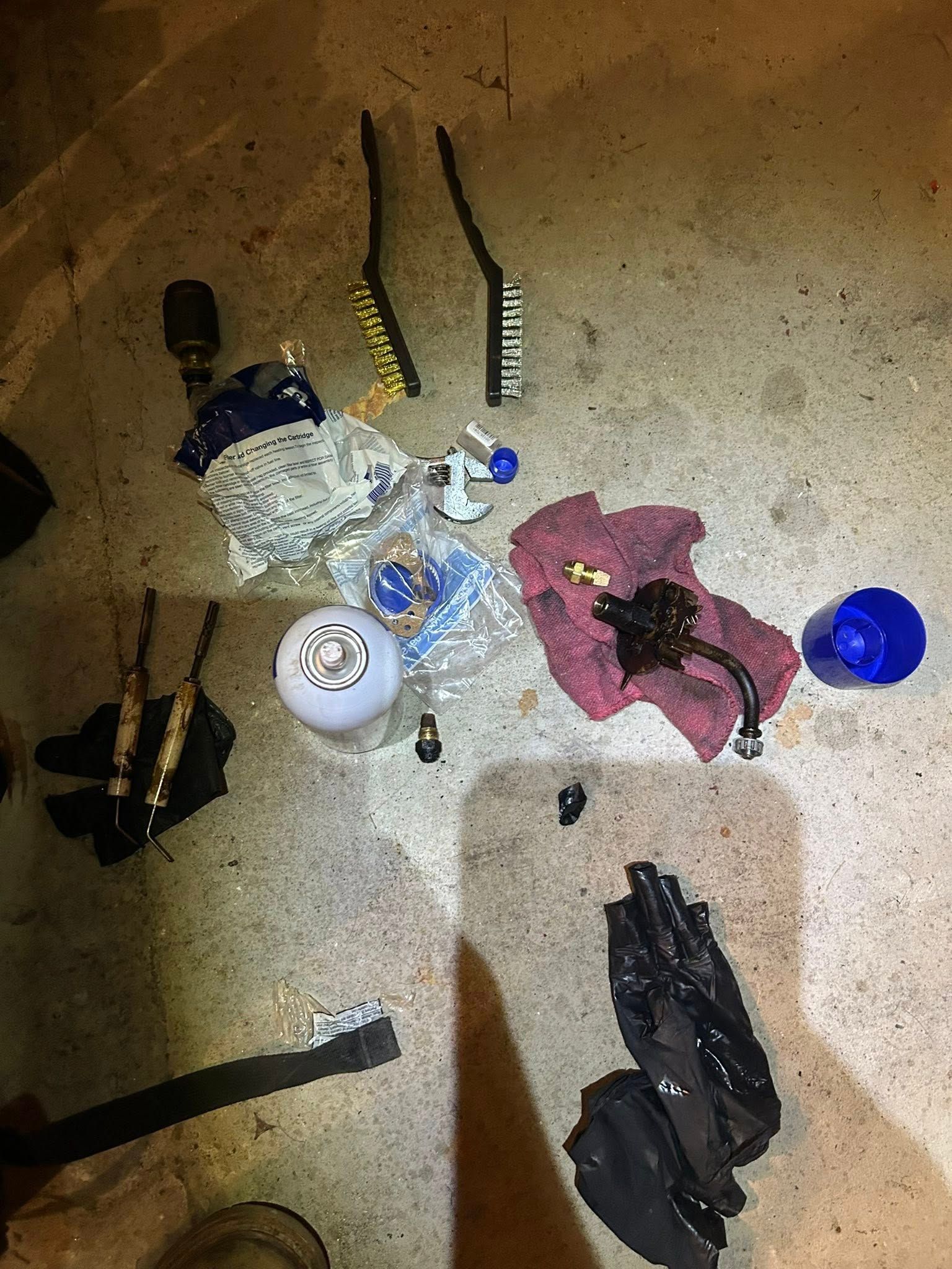 A collection of automotive maintenance tools, including brushes, a shift knob, and greasy rags, scattered on a concrete floor.