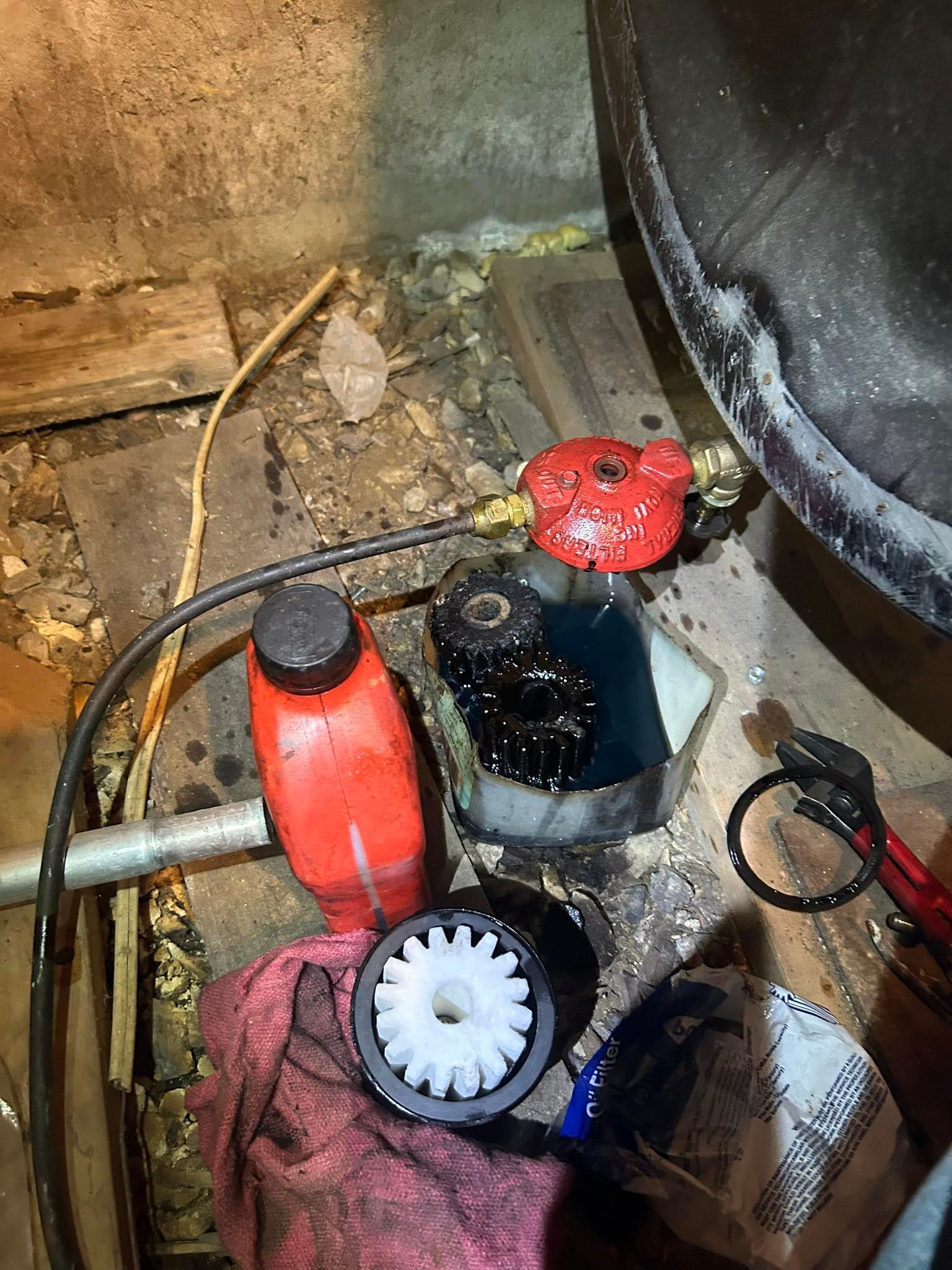 A cluttered workspace with a red regulator, a red plastic bottle, a white gear, and a black component in a basin.