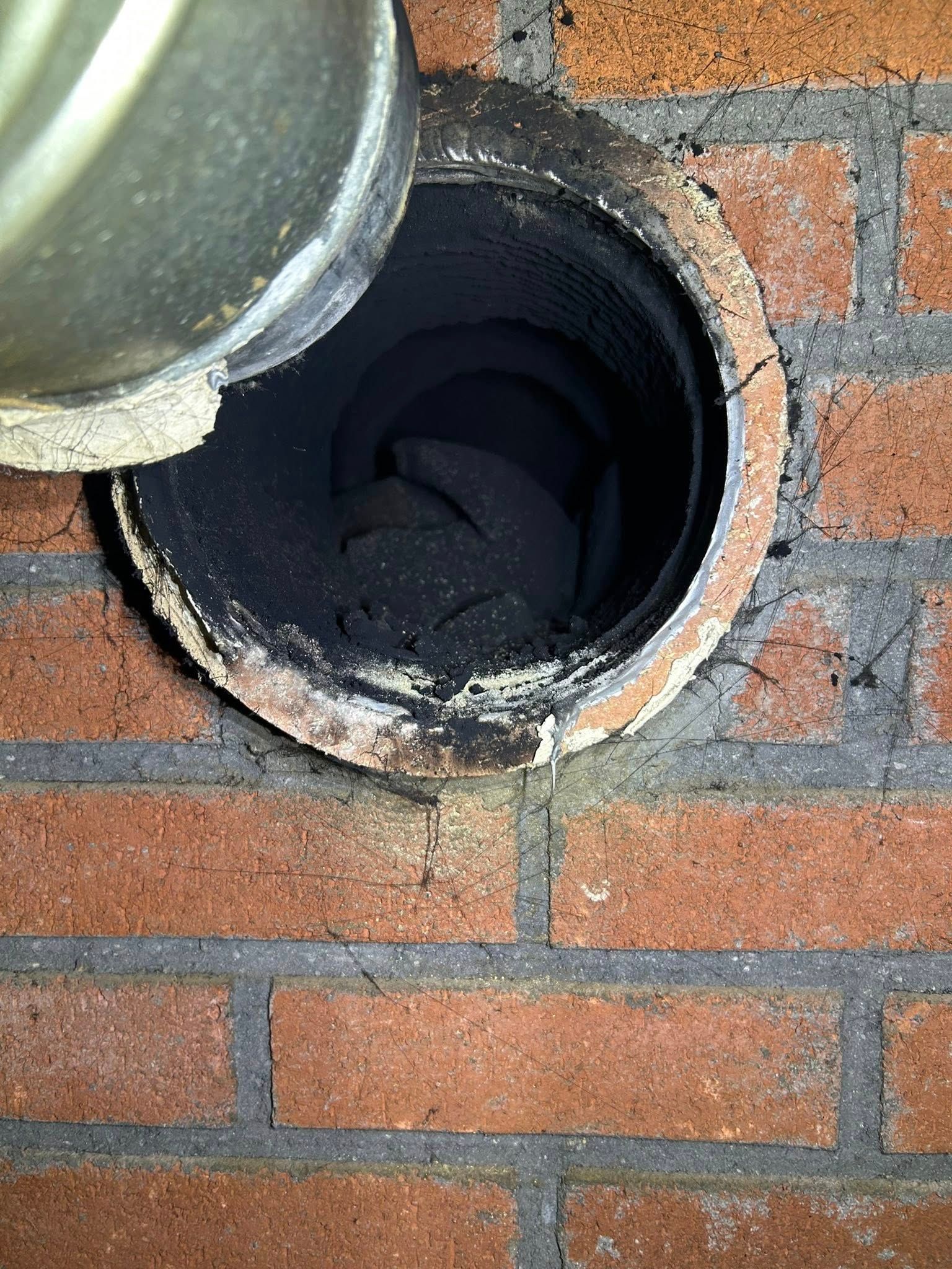 A close-up view of an open, dark chimney flue with significant creosote buildup, set into a red brick wall.