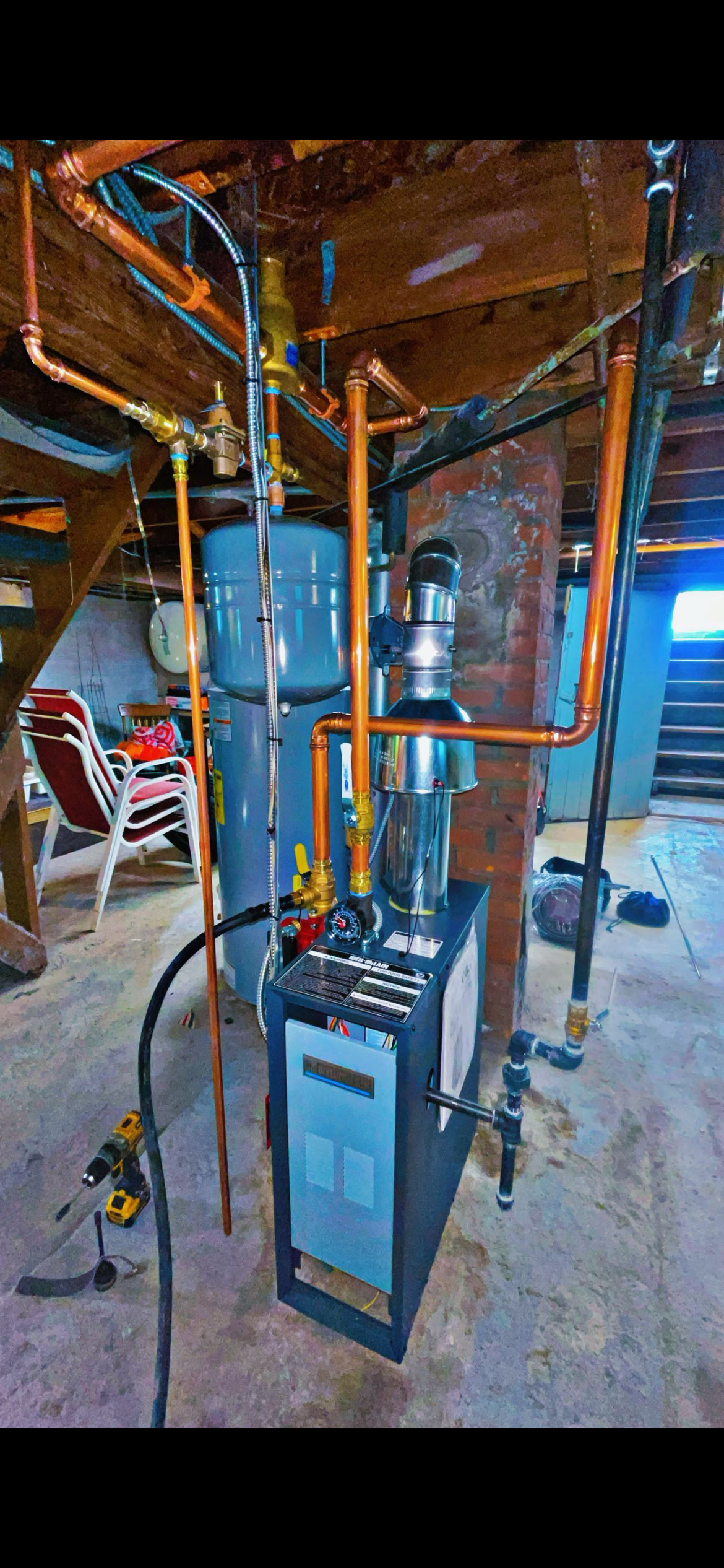 A vertical shot of a residential boiler and blue expansion tank in a basement with exposed wooden ceiling beams.