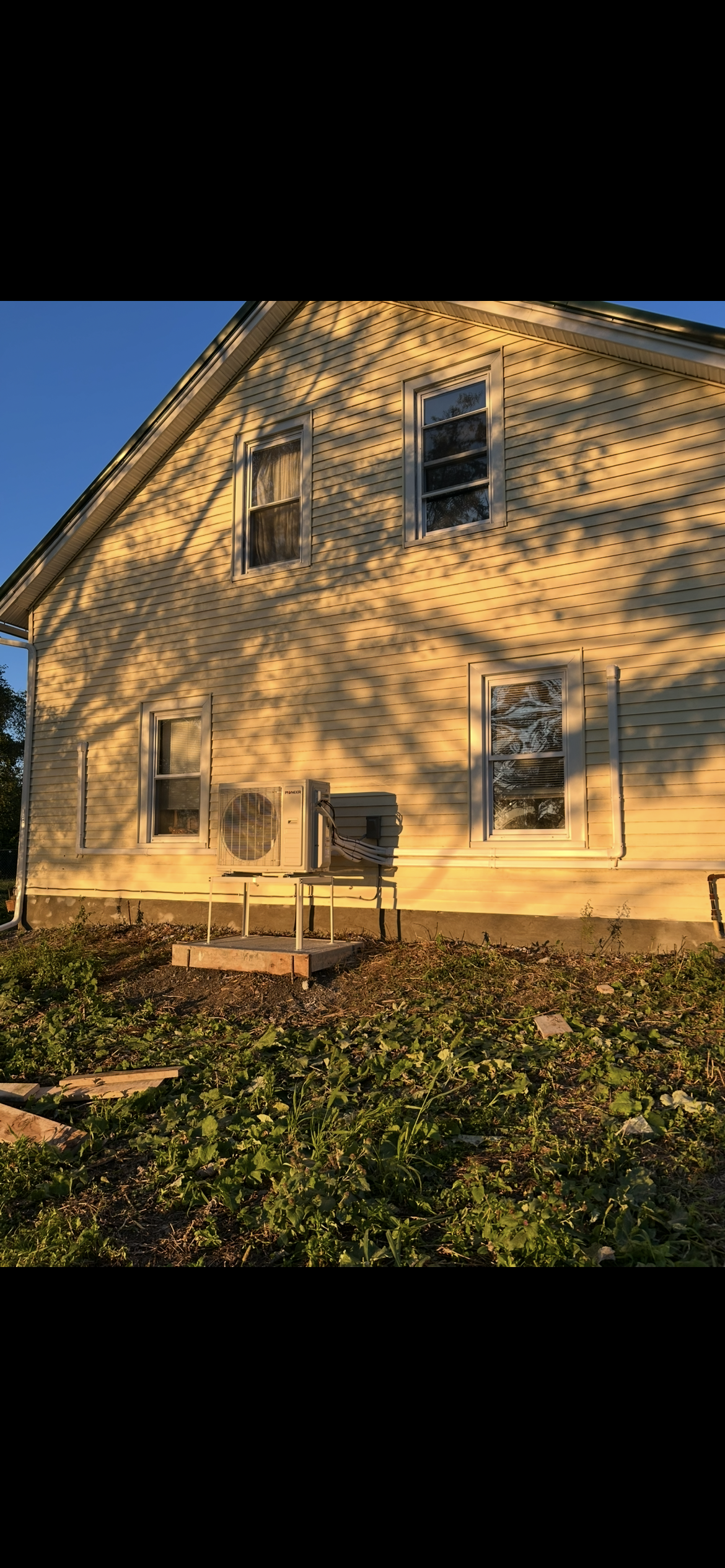 A yellow house side at sunset with dappled shadows from a nearby tree casting patterns across the wall and windows.
