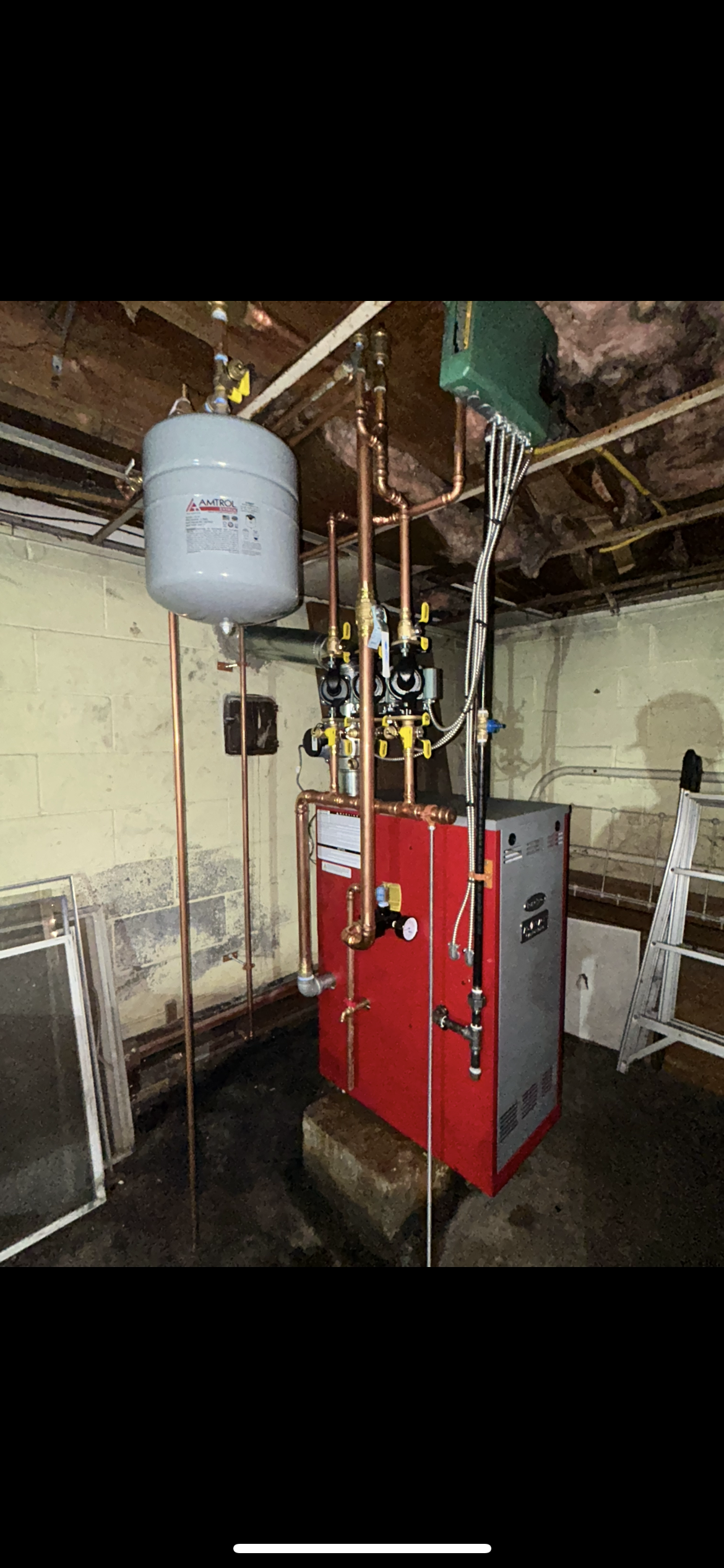 A red and gray boiler with copper pipes and a gray expansion tank located in an unfinished basement.